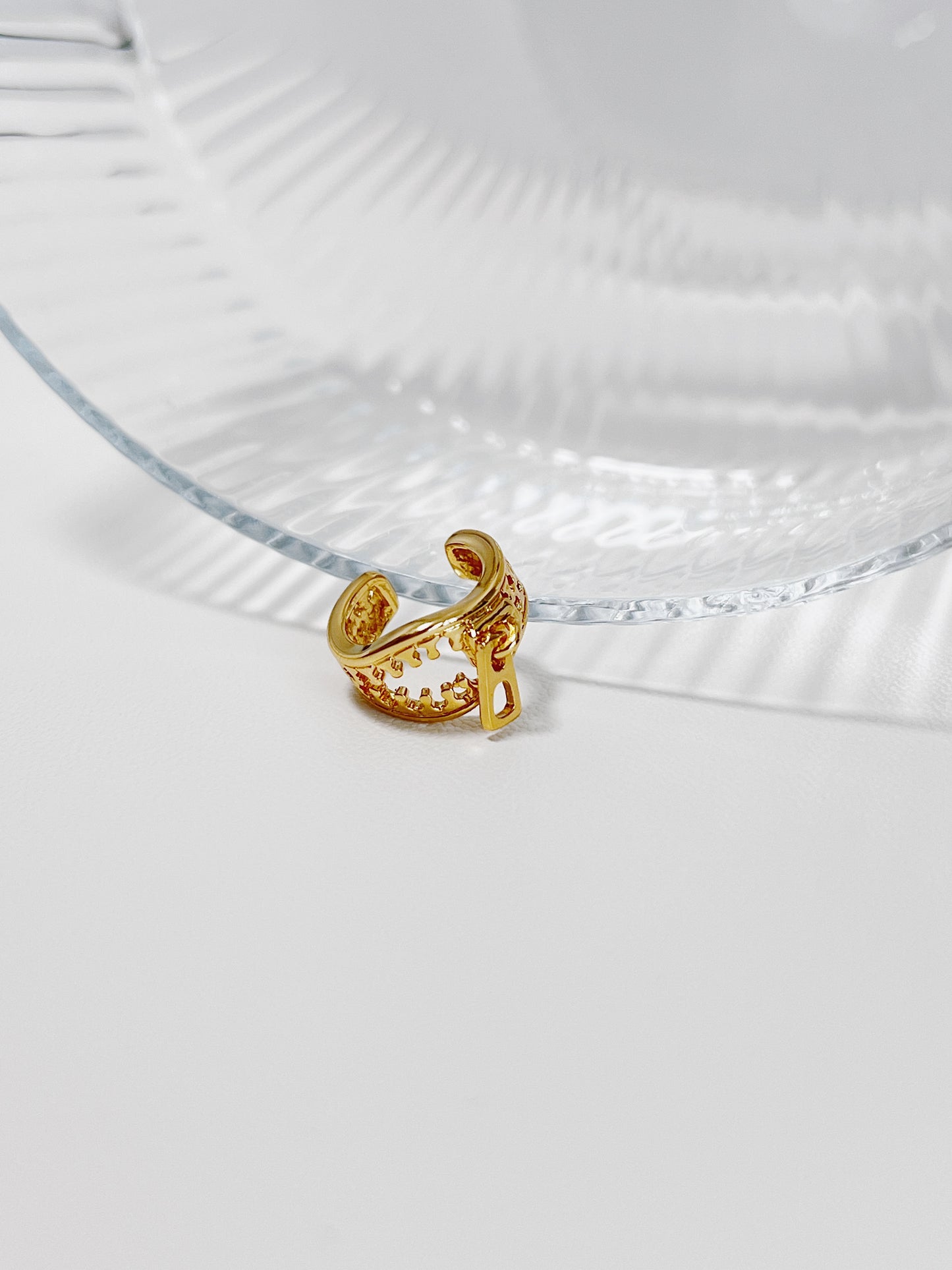 Gold ear cuff with intricate zipper design on a clear glass surface