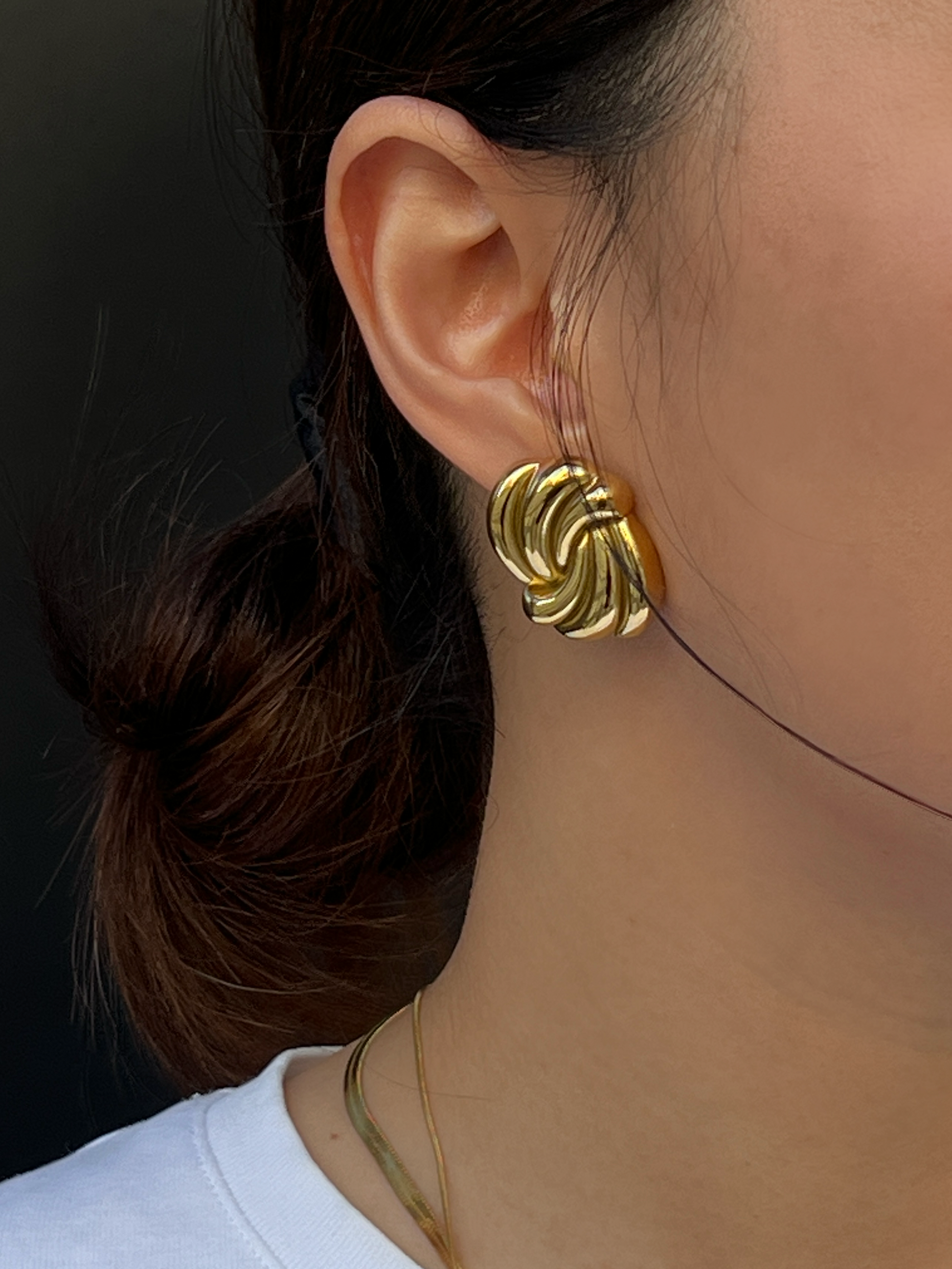 Close-up of a person wearing chunky gold stud earrings with a plain background