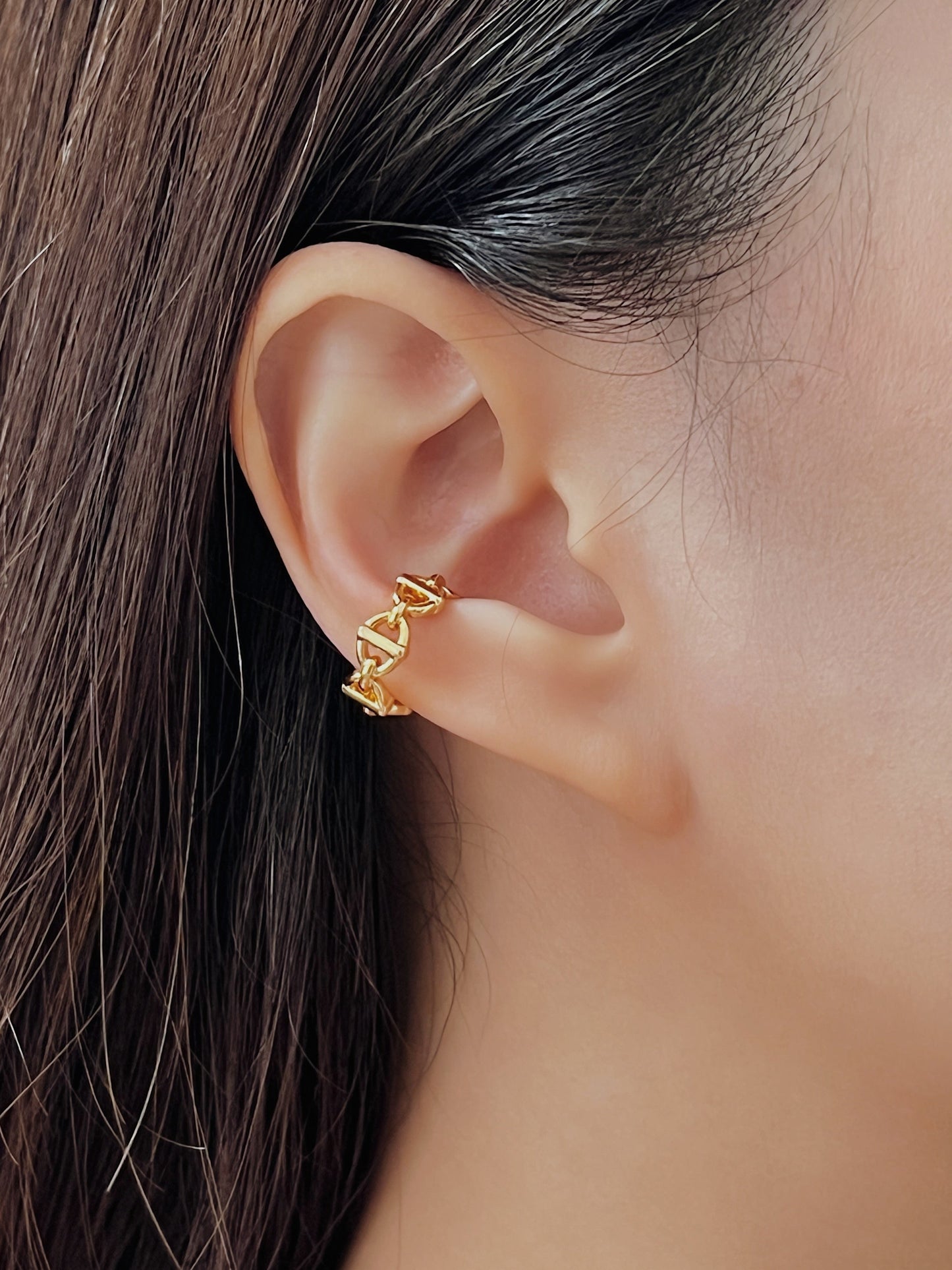 Close-up of an ear wearing a gold chain link ear cuff