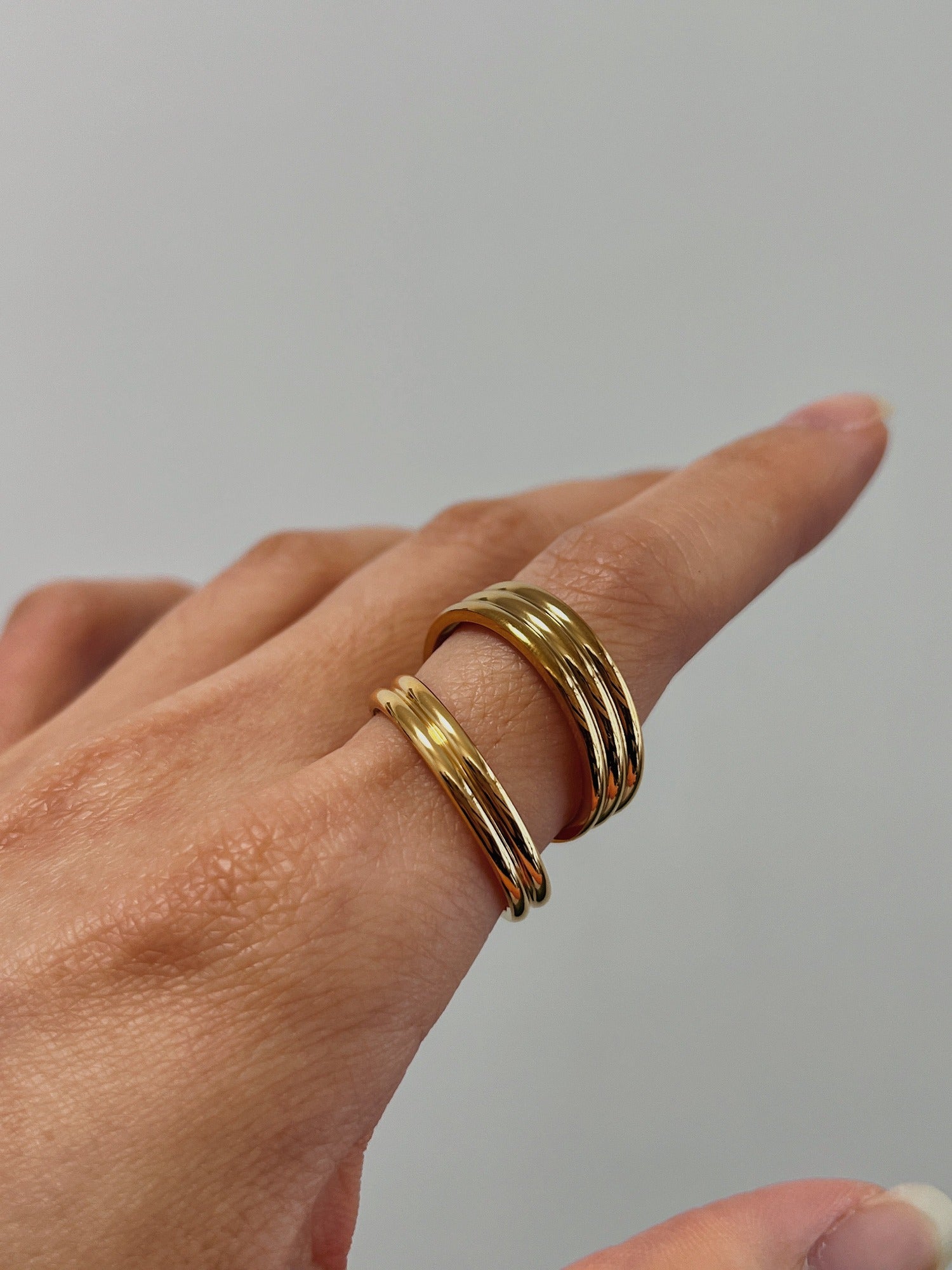 Hand model wearing thick and slim Kori gold ribbed ring on index finger