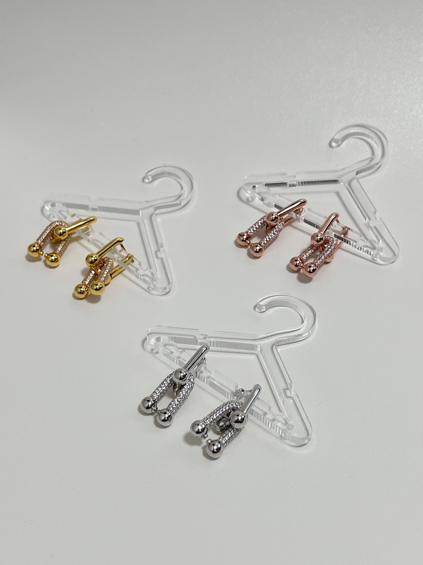 luxurious link earrings hang on transparent mini jewelry hangers and displayed on a white surface. 