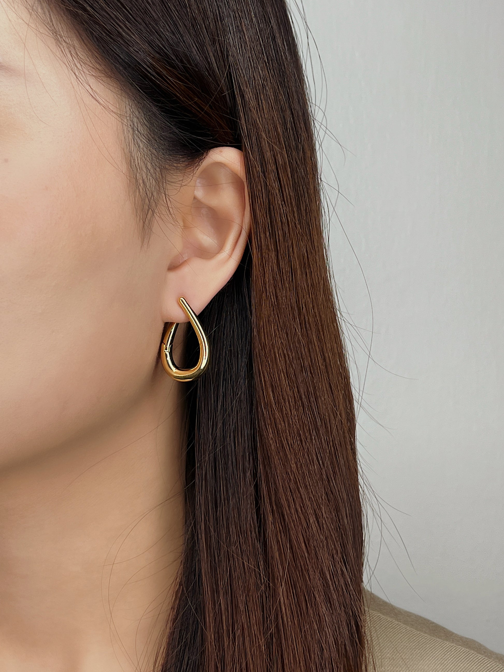Close-up of a person wearing a gold twist hoop earring with a neutral background