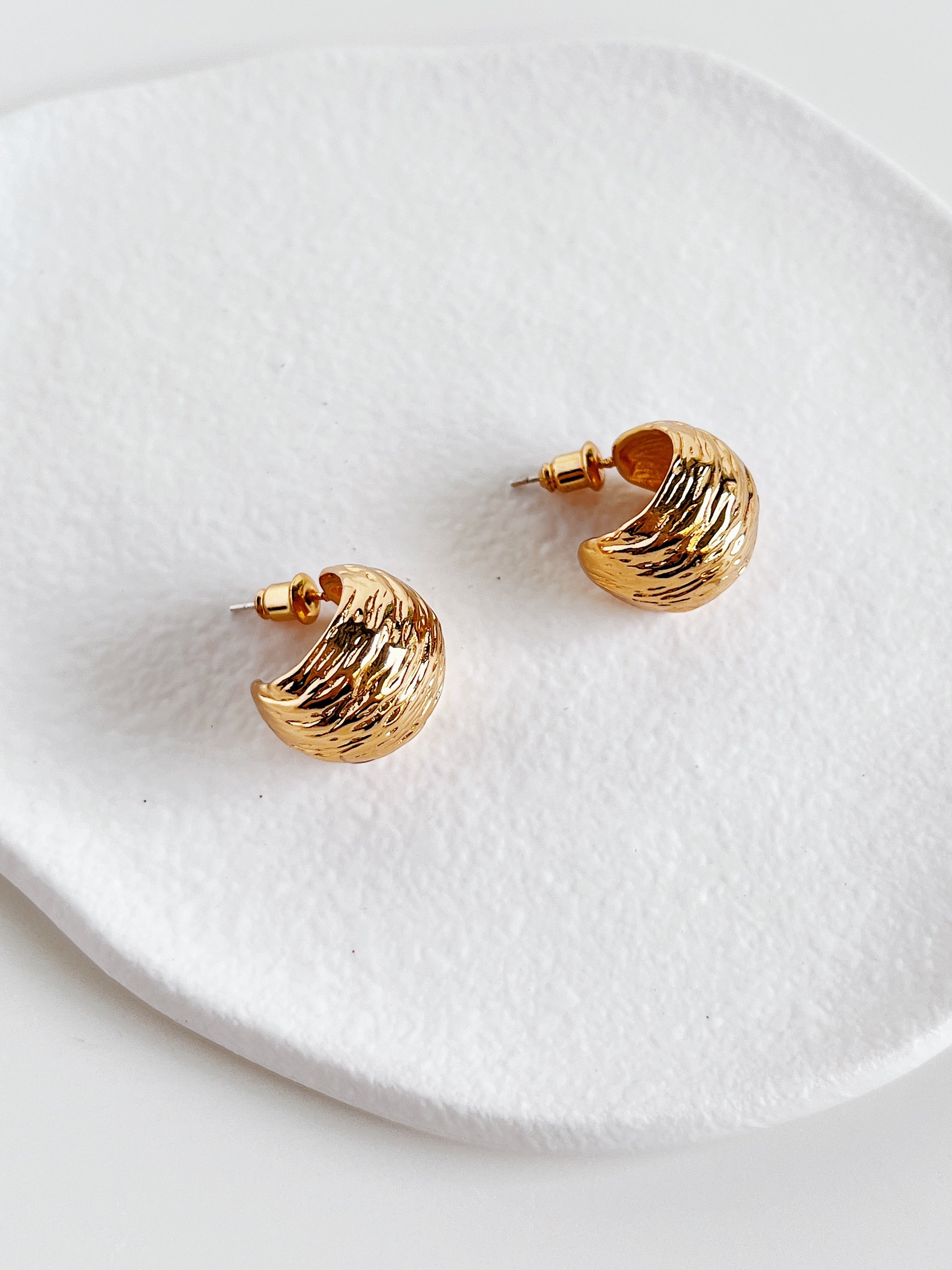 Gold hoop earrings on a white textured plate