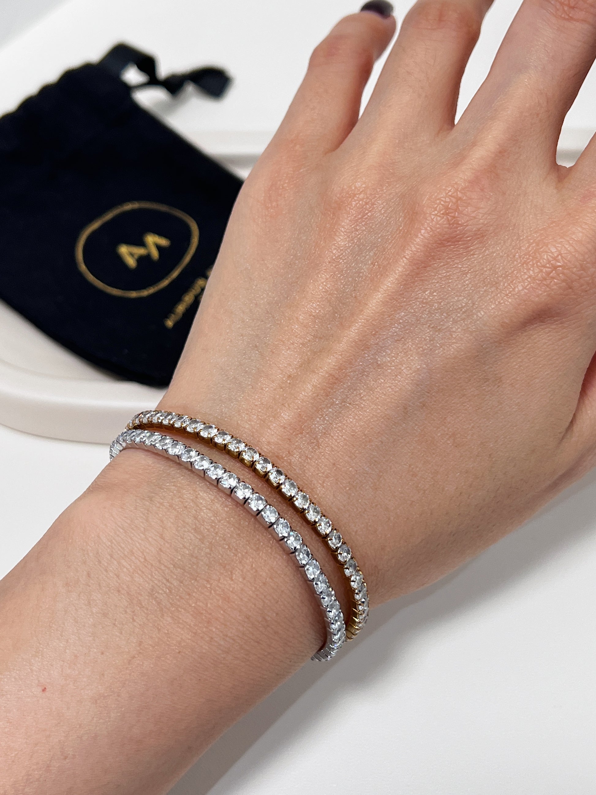 Hand wearing a silver diamond bracelet with a black pouch in the background