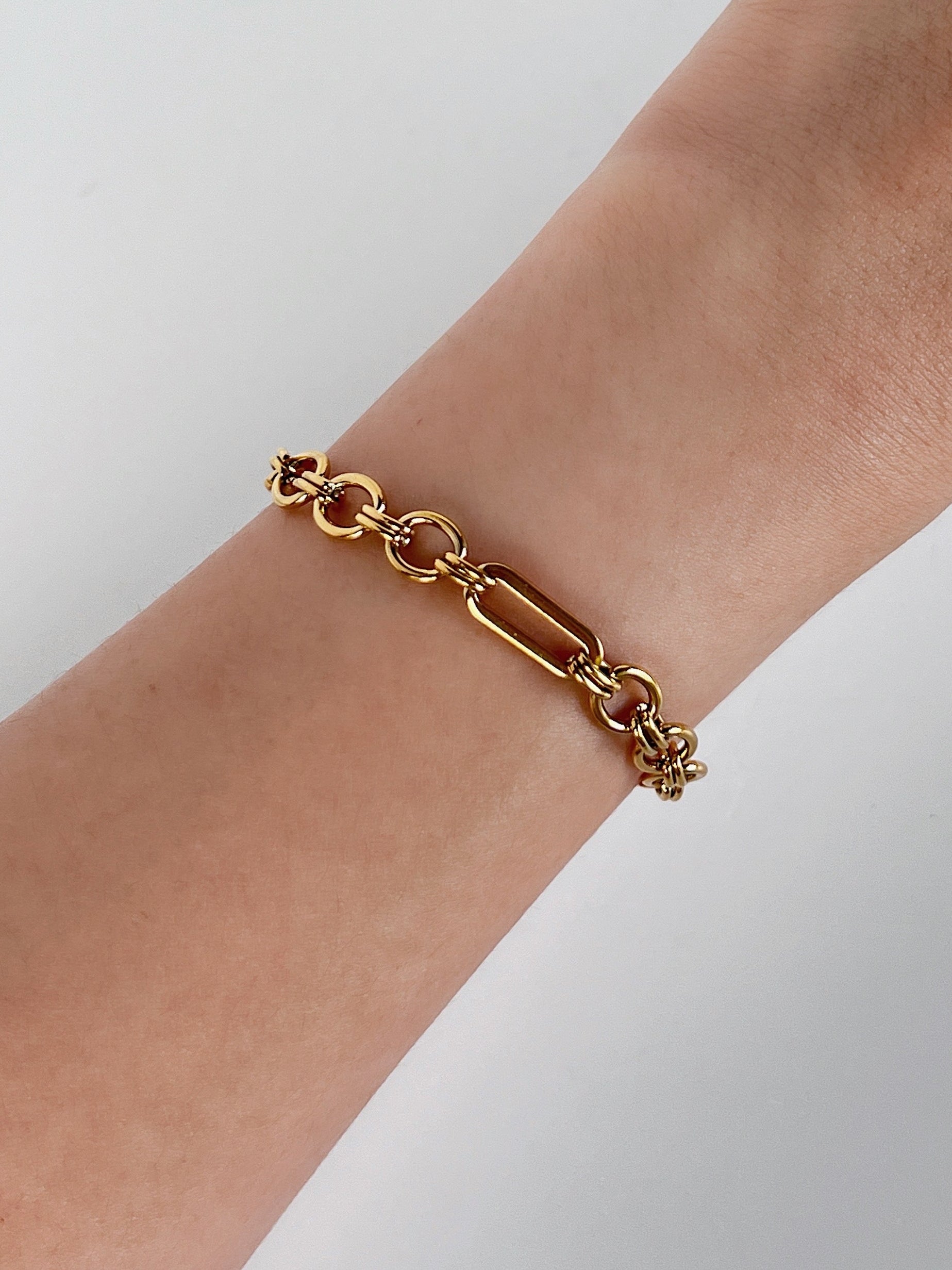 Gold chain bracelet on a wrist against a light background