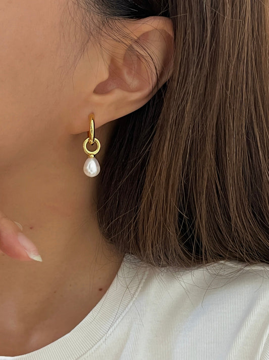 A woman wearing a dainty gold dangle pearl earrings, pairs with white outfit for a simple elegant look