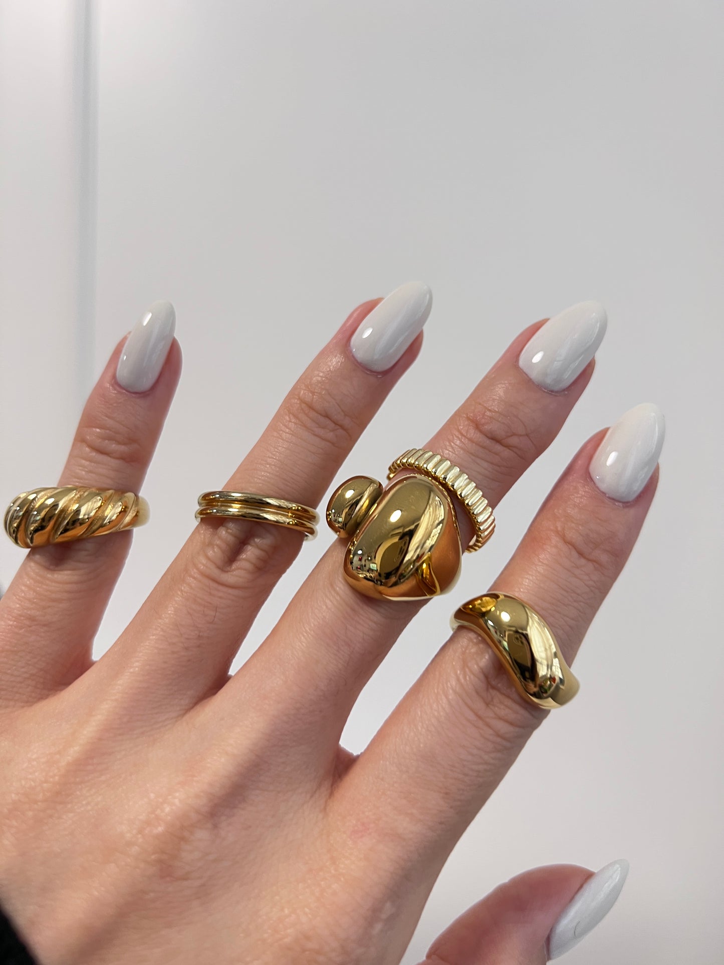 Hand wearing multiple gold rings with a plain background