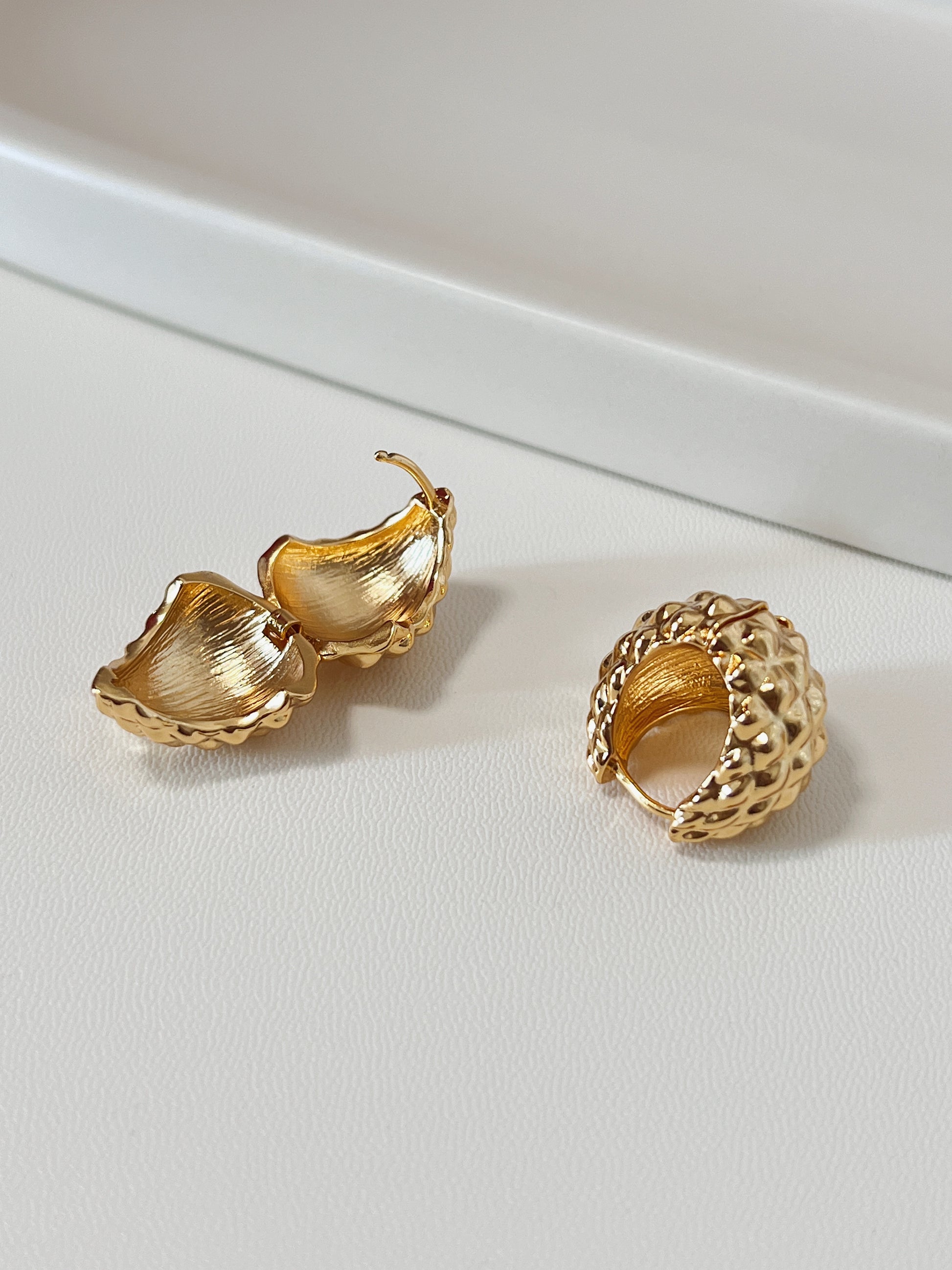 Gold spike hoop earrings on a light gray surface with a beige background