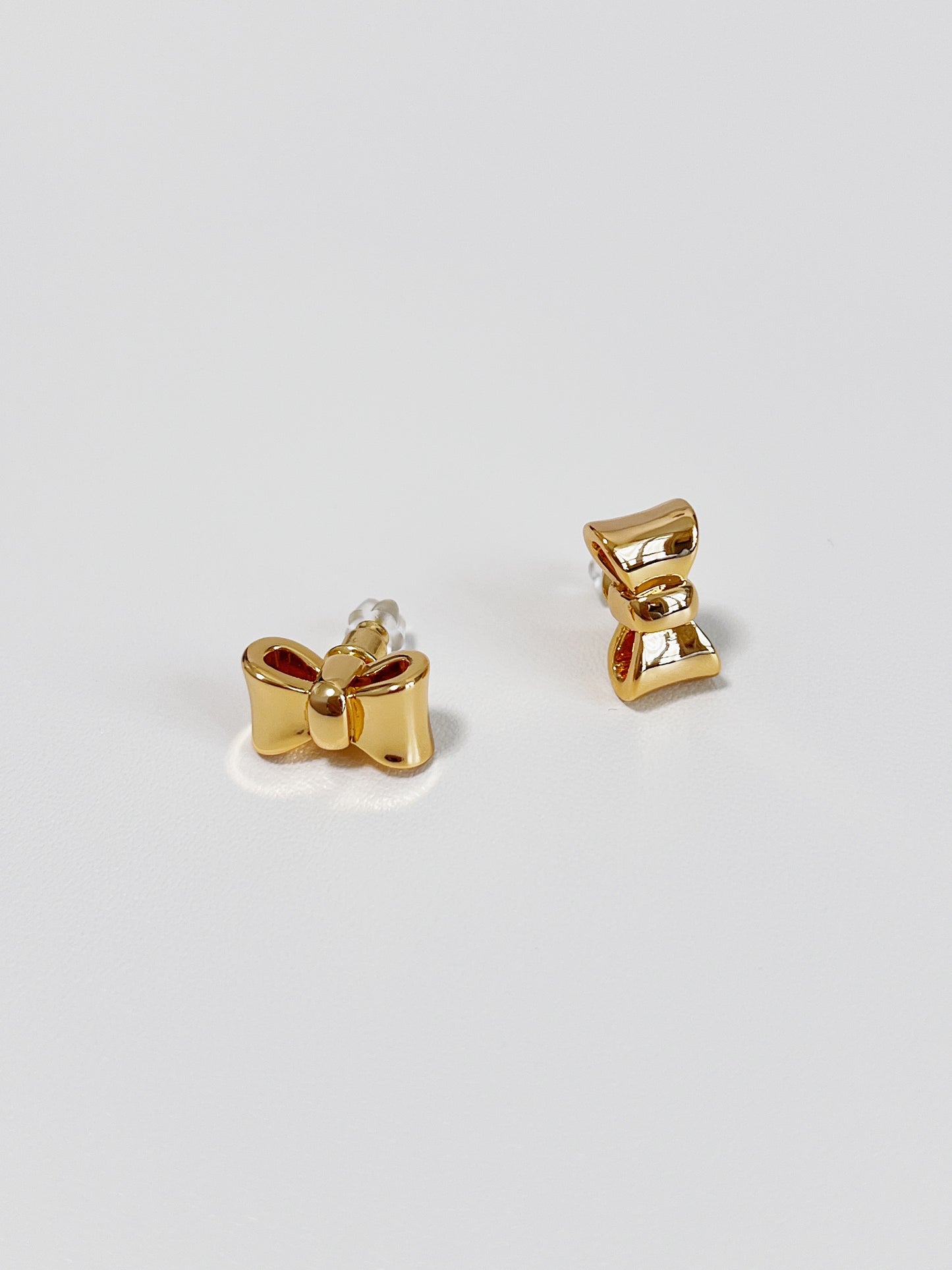 Gold bow-shaped earrings on a light gray background