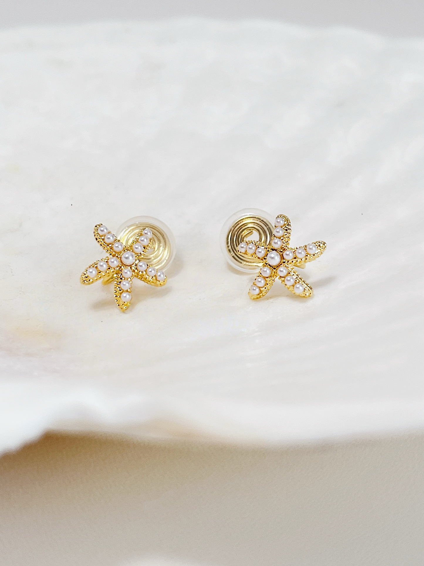 Gold starfish clip on earrings on a white shell background
