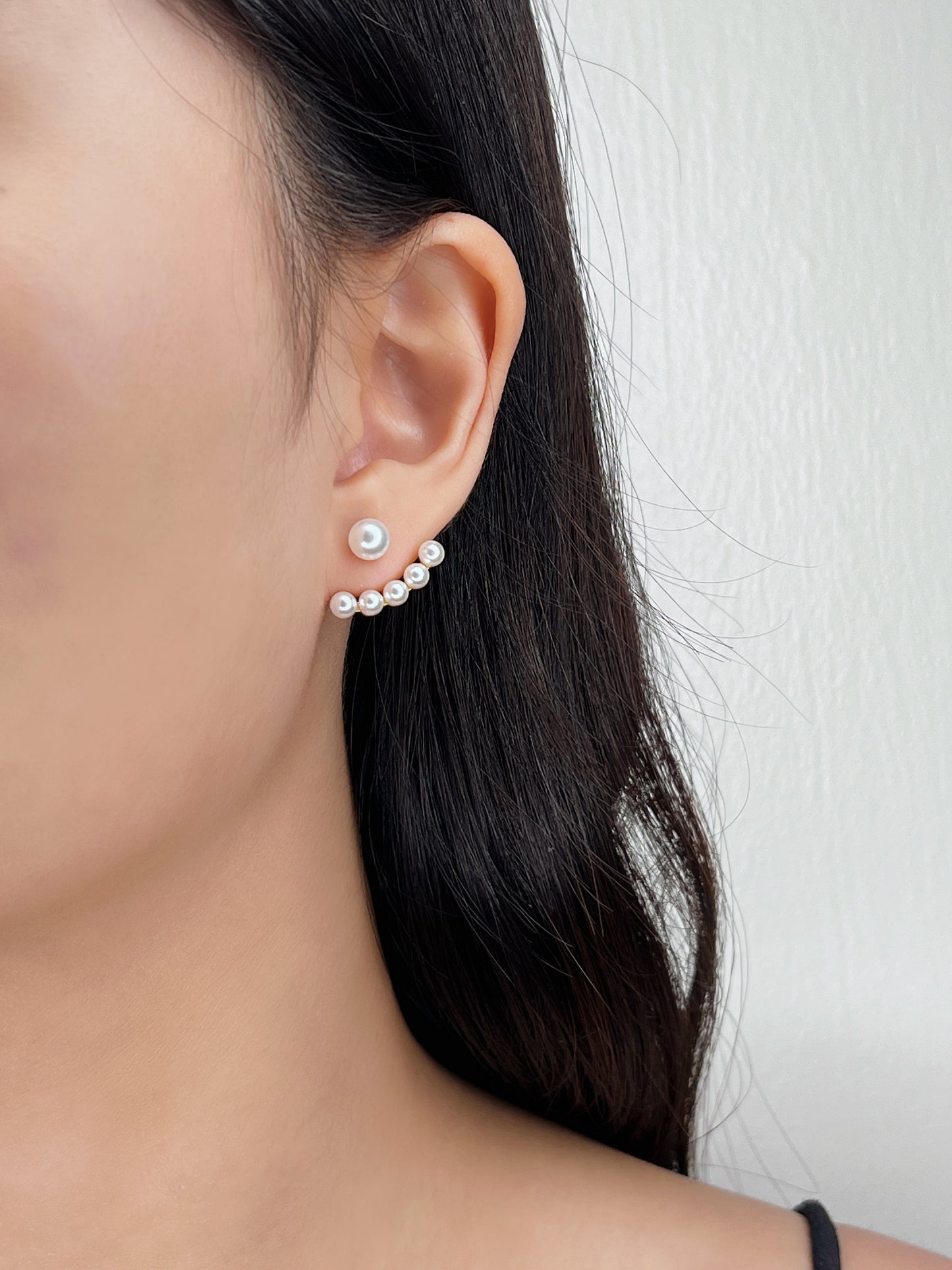 Close-up of a person wearing pearl stud earrings with a neutral background