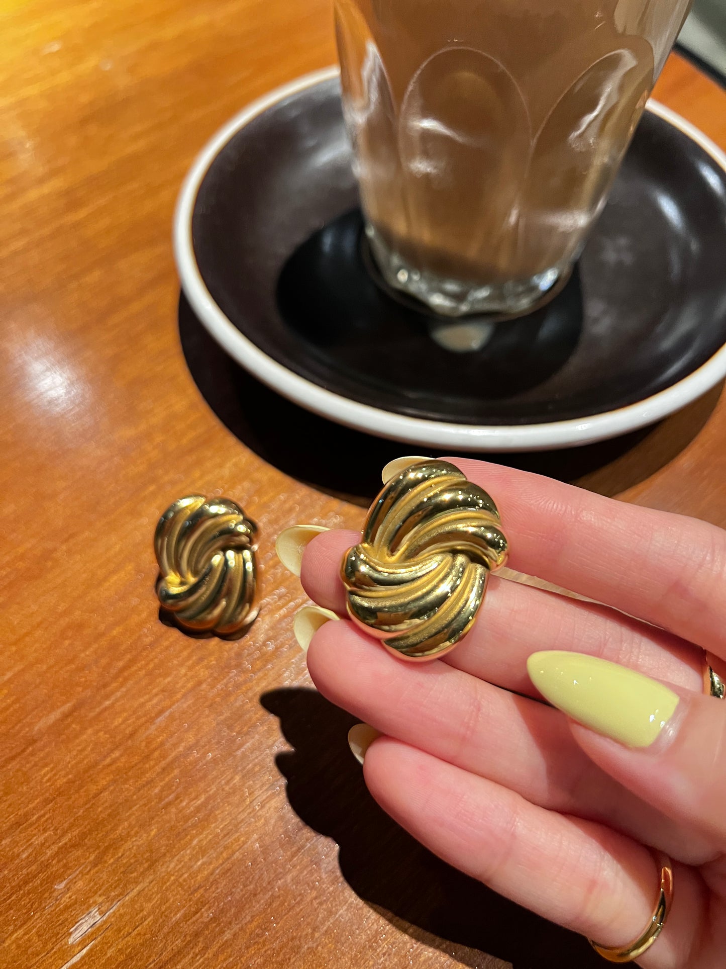 Gold earrings being held above a black bowl on a wooden surface