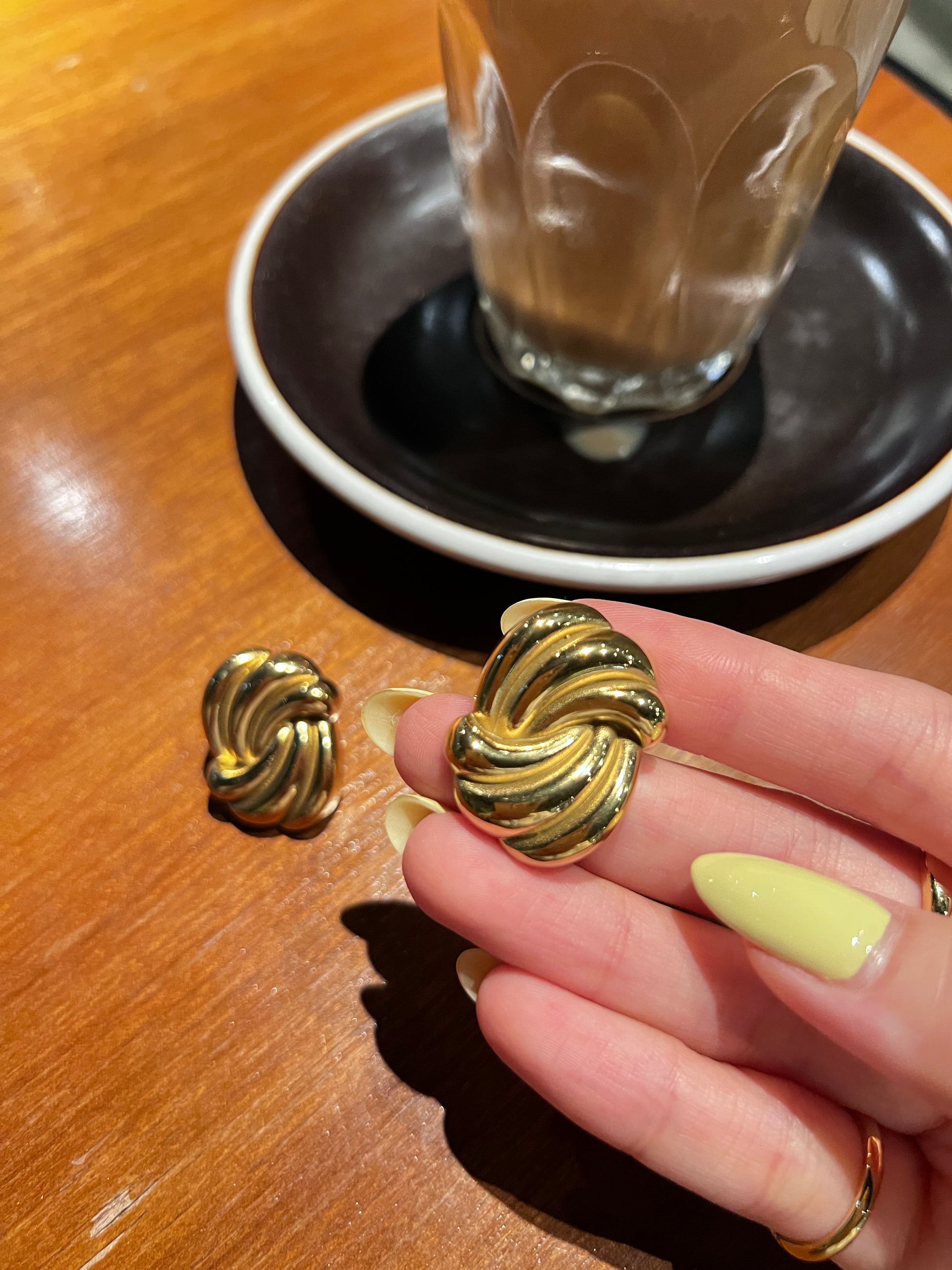 Gold earrings being held above a black bowl on a wooden surface