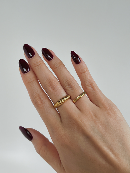 Hand with gold ring and dark nail polish on a plain background