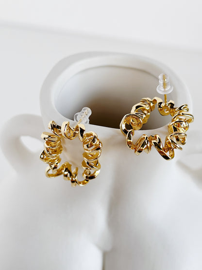 Gold curly earrings on a white stand with a white background