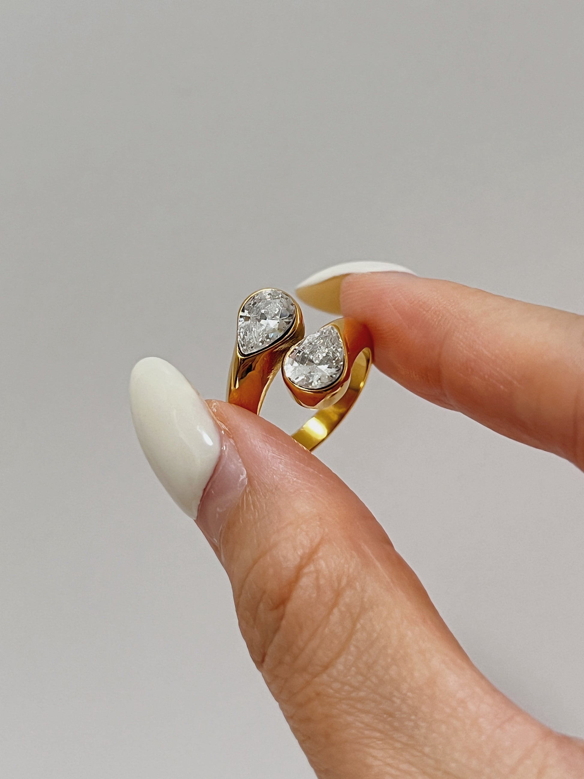 Gold ring with two diamonds held by a hand against a neutral background