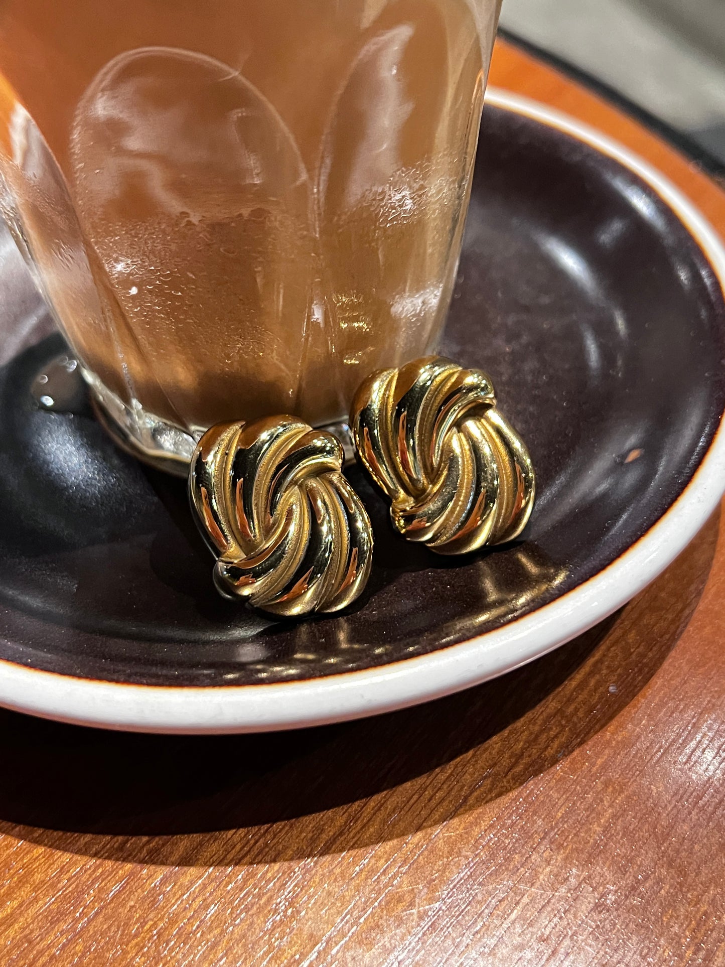 Gold twist earrings on a dark surface with a wooden background