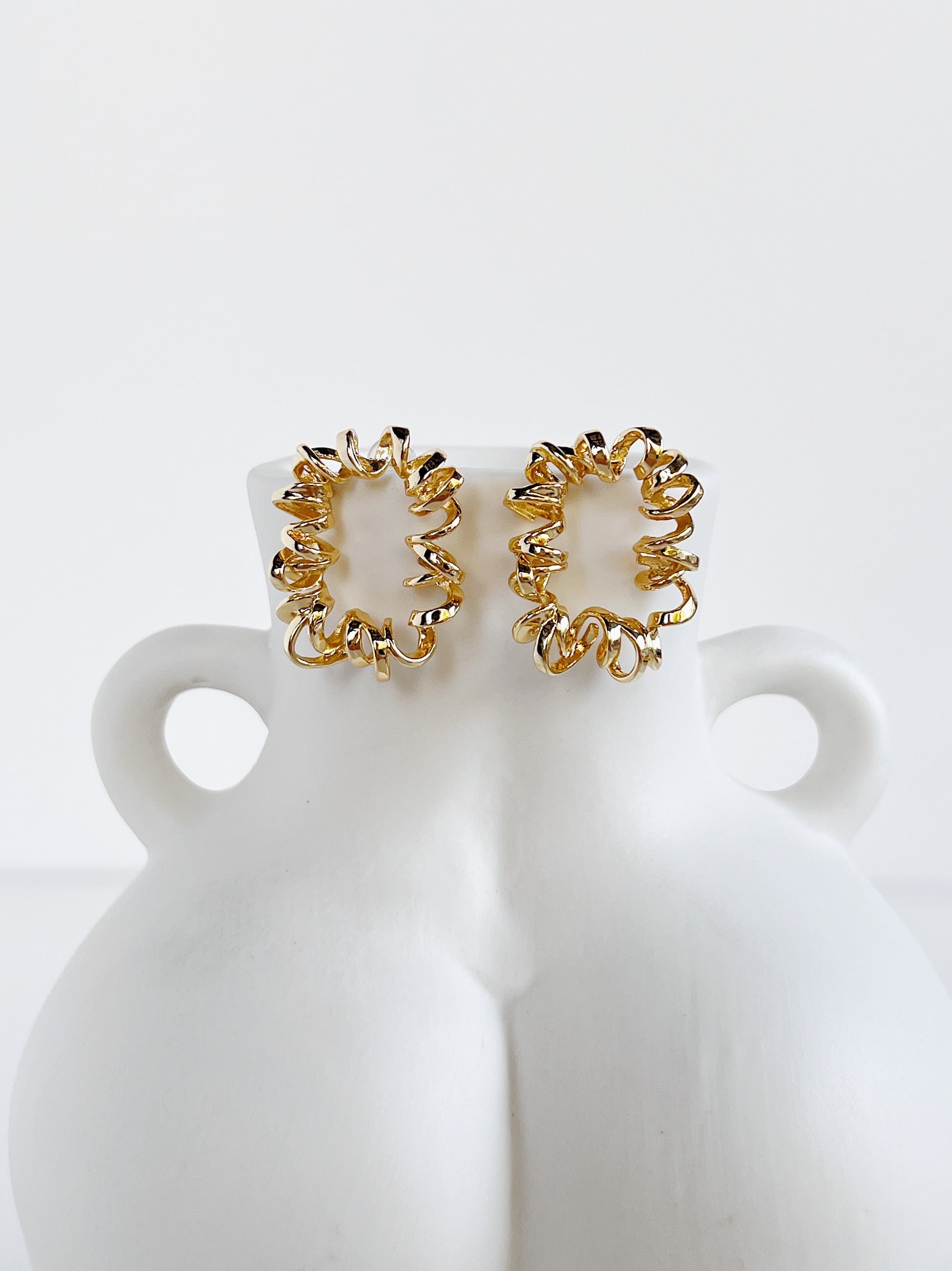 Gold curly earrings on a white bust