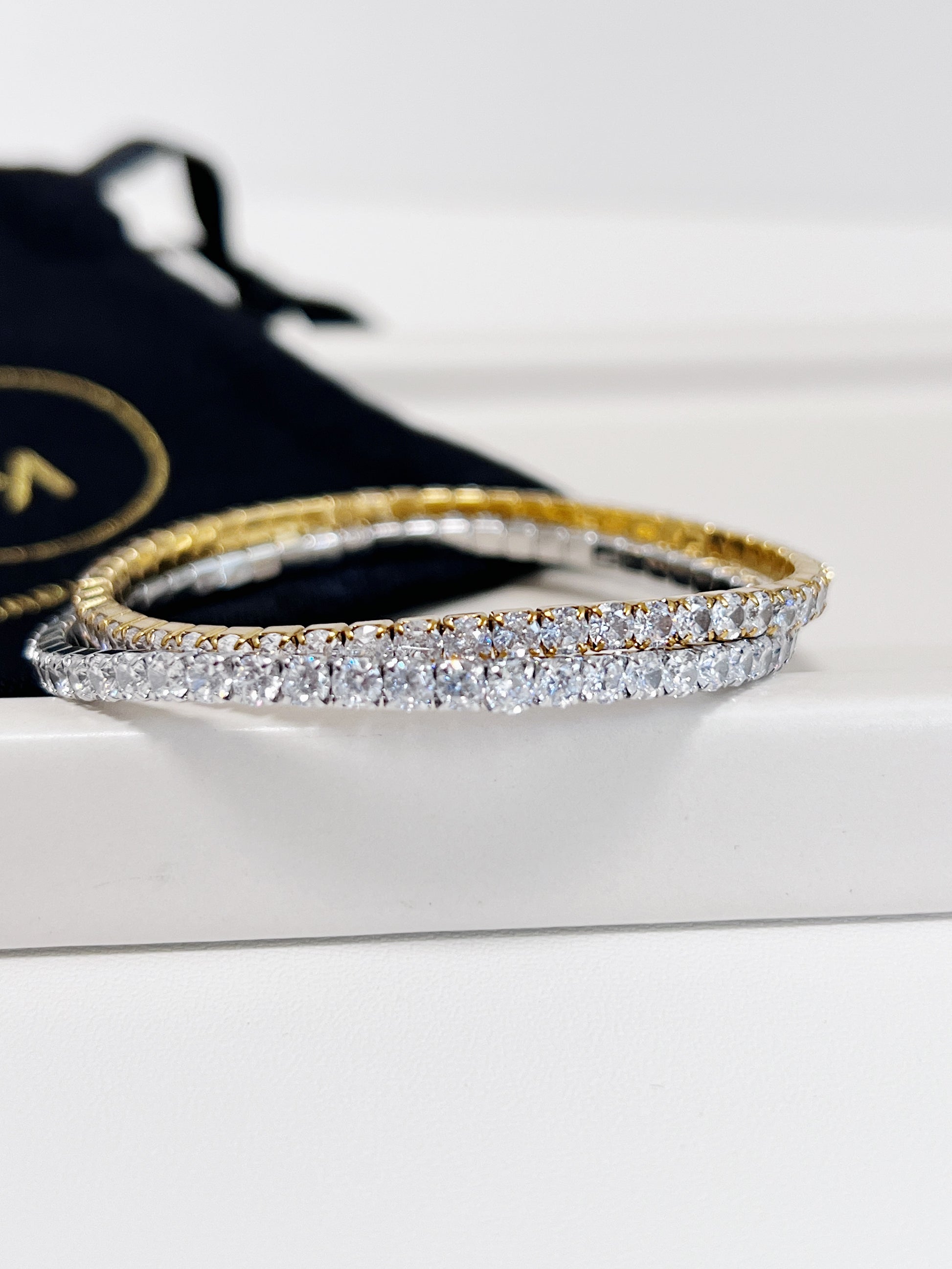 Gold and silver tennis bracelet on a white surface with a black pouch in the background