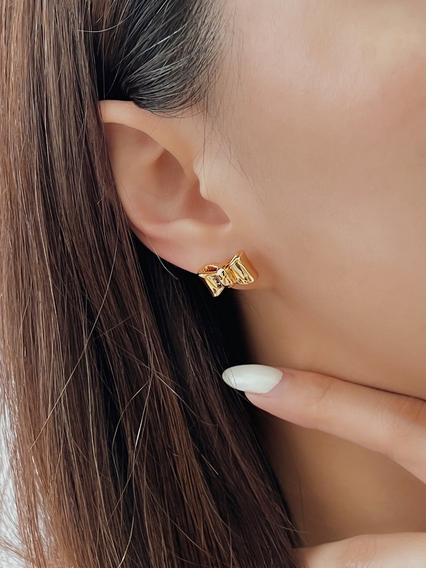 Close-up of an ear wearing a bow gold stud earring with a blurred background