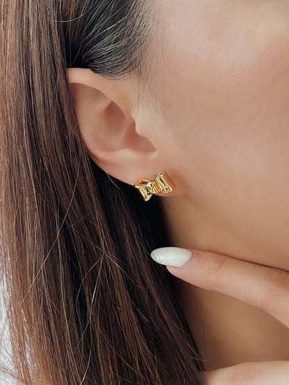 Close-up of an ear wearing a bow gold stud earring with a blurred background