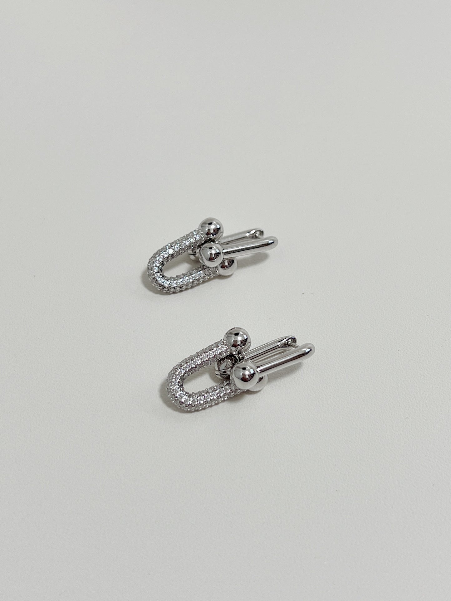 Sophisticated earrings design showcasing silver material, diamond inlay, and interlock motif, display on a white surface.