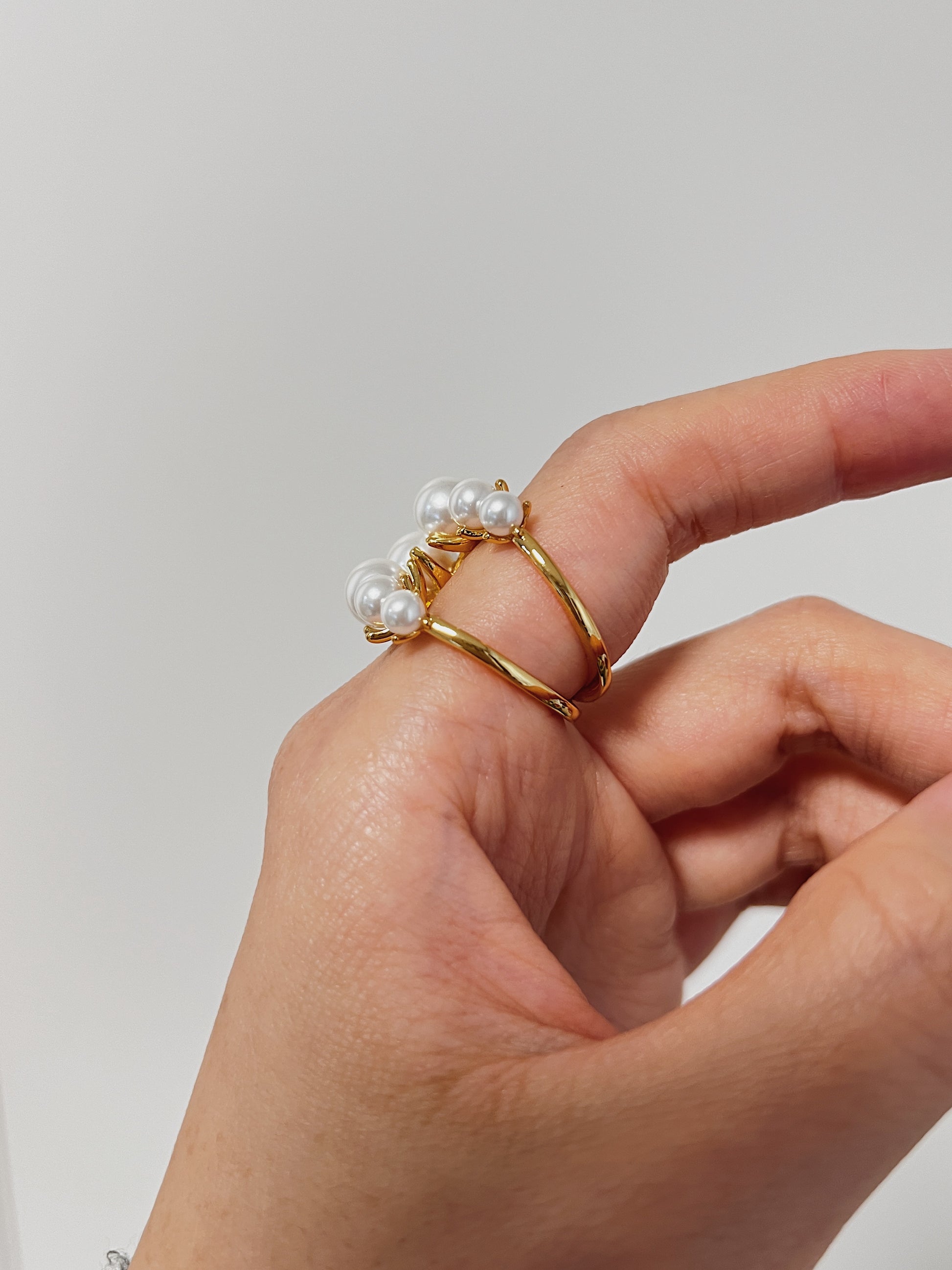 Gold ring with pearls being worn on a finger against a plain background