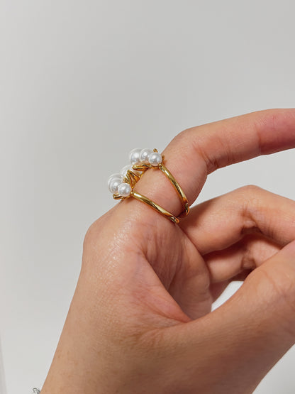 Gold ring with pearls being worn on a finger against a plain background