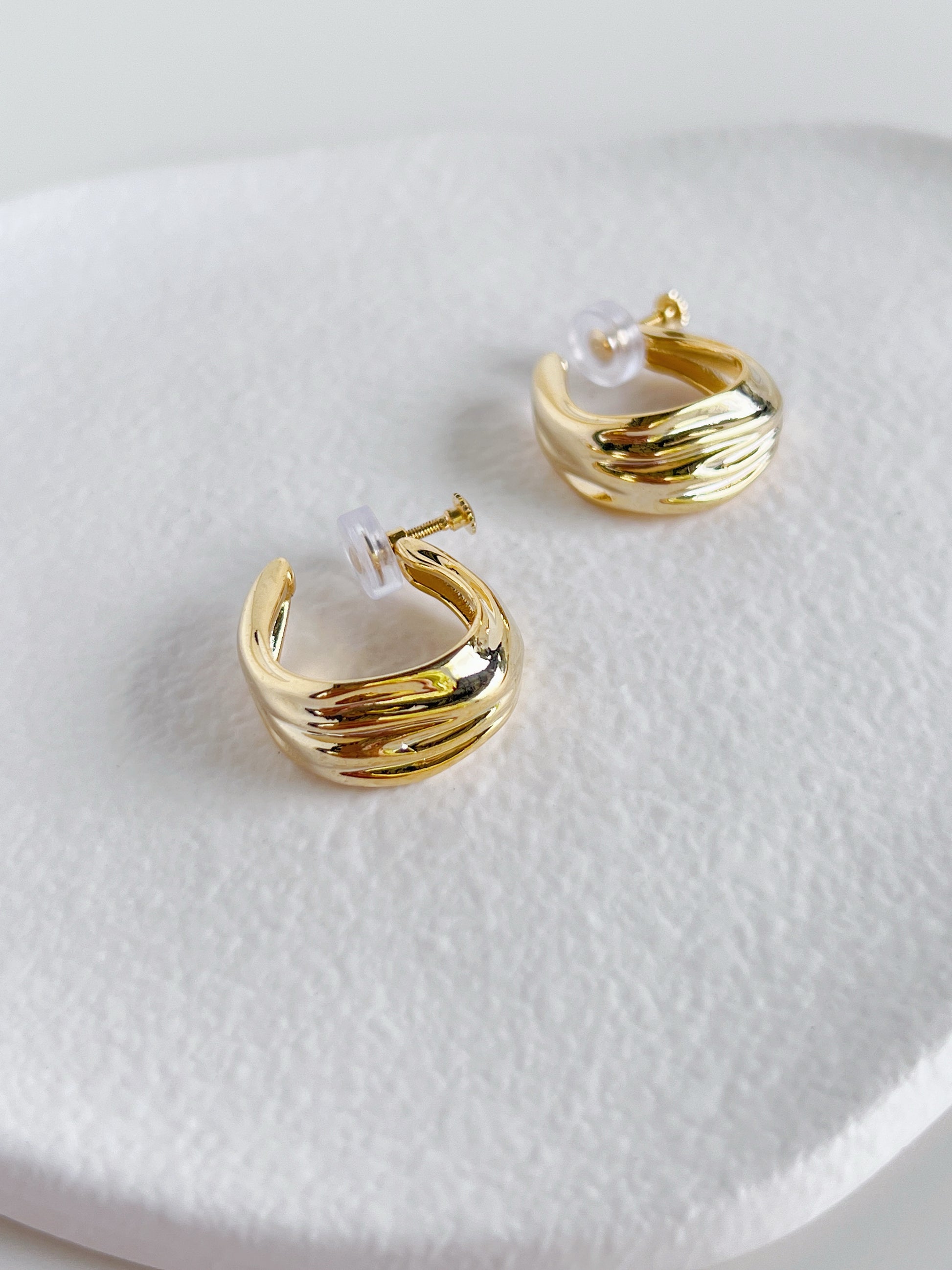 Close up of gold textured clip on hoop earrings on a ceramic white surface