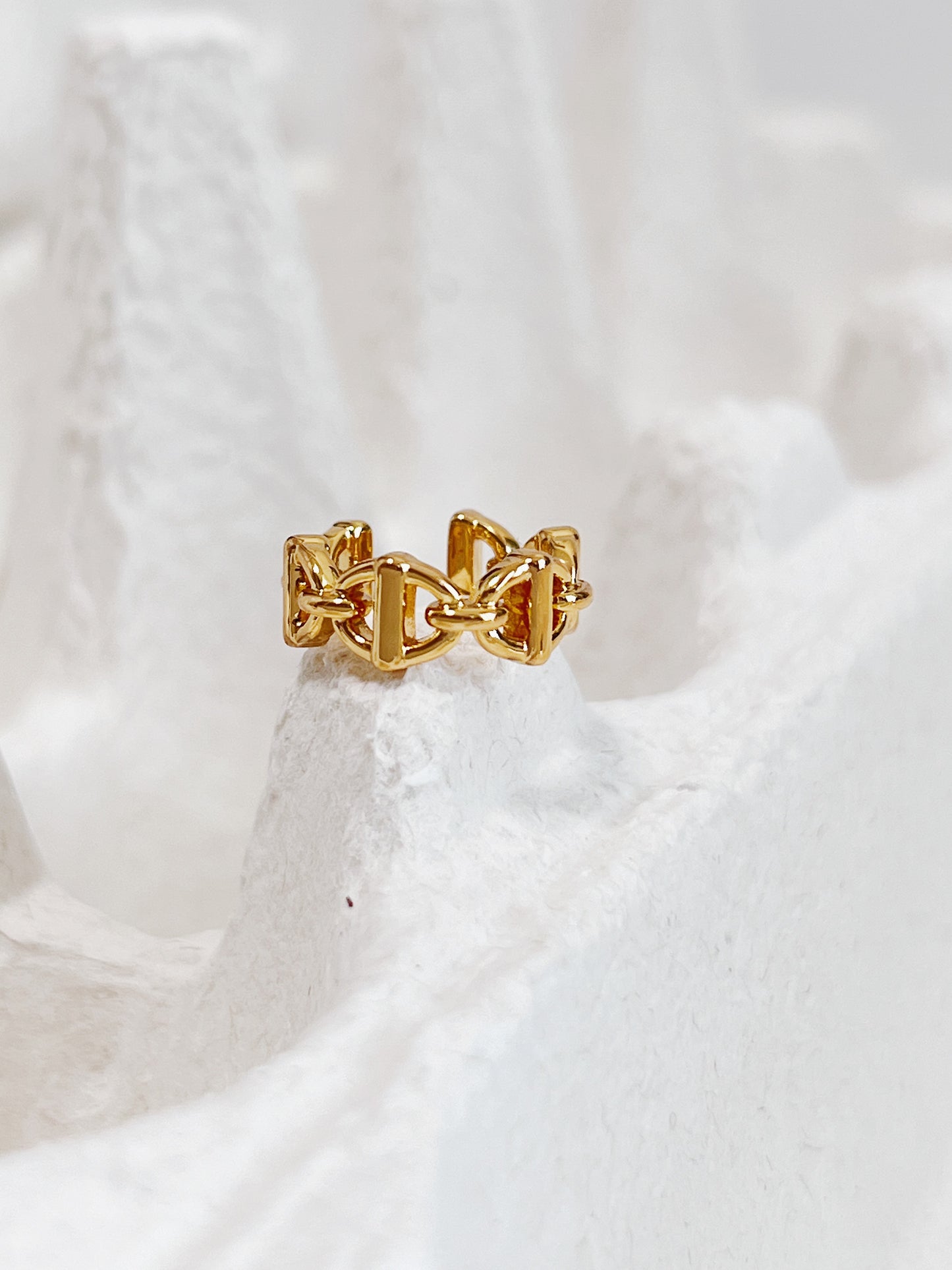 Gold chain-link ear cuff on a textured white surface