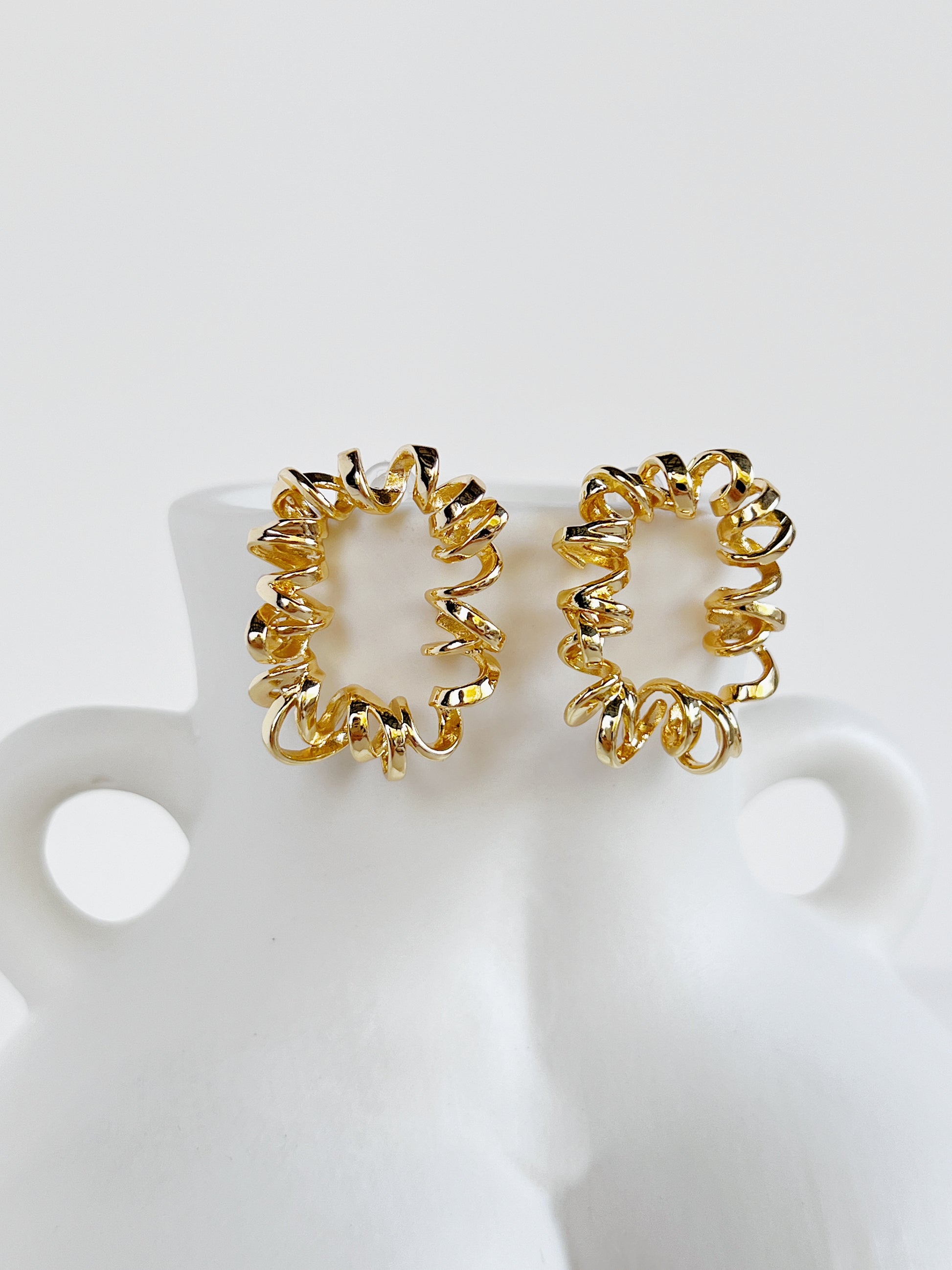 Pair of gold curly stud earrings on a white stand