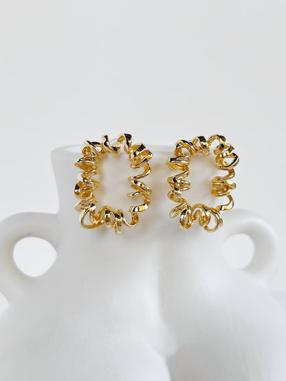 Pair of gold curly stud earrings on a white stand
