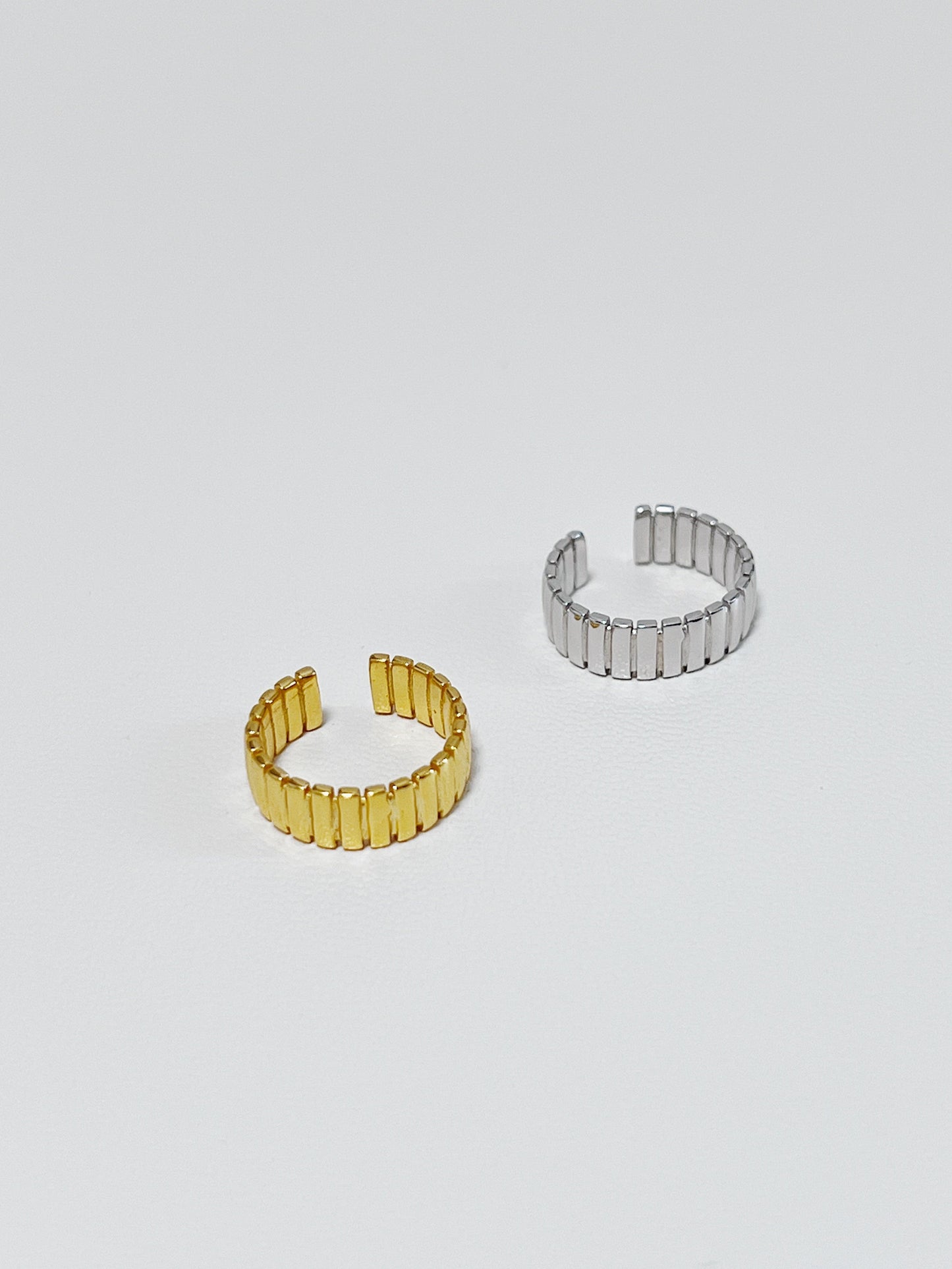 Two gold and silver ribbed ear cuff made of S925 sterling silver on a light gray background