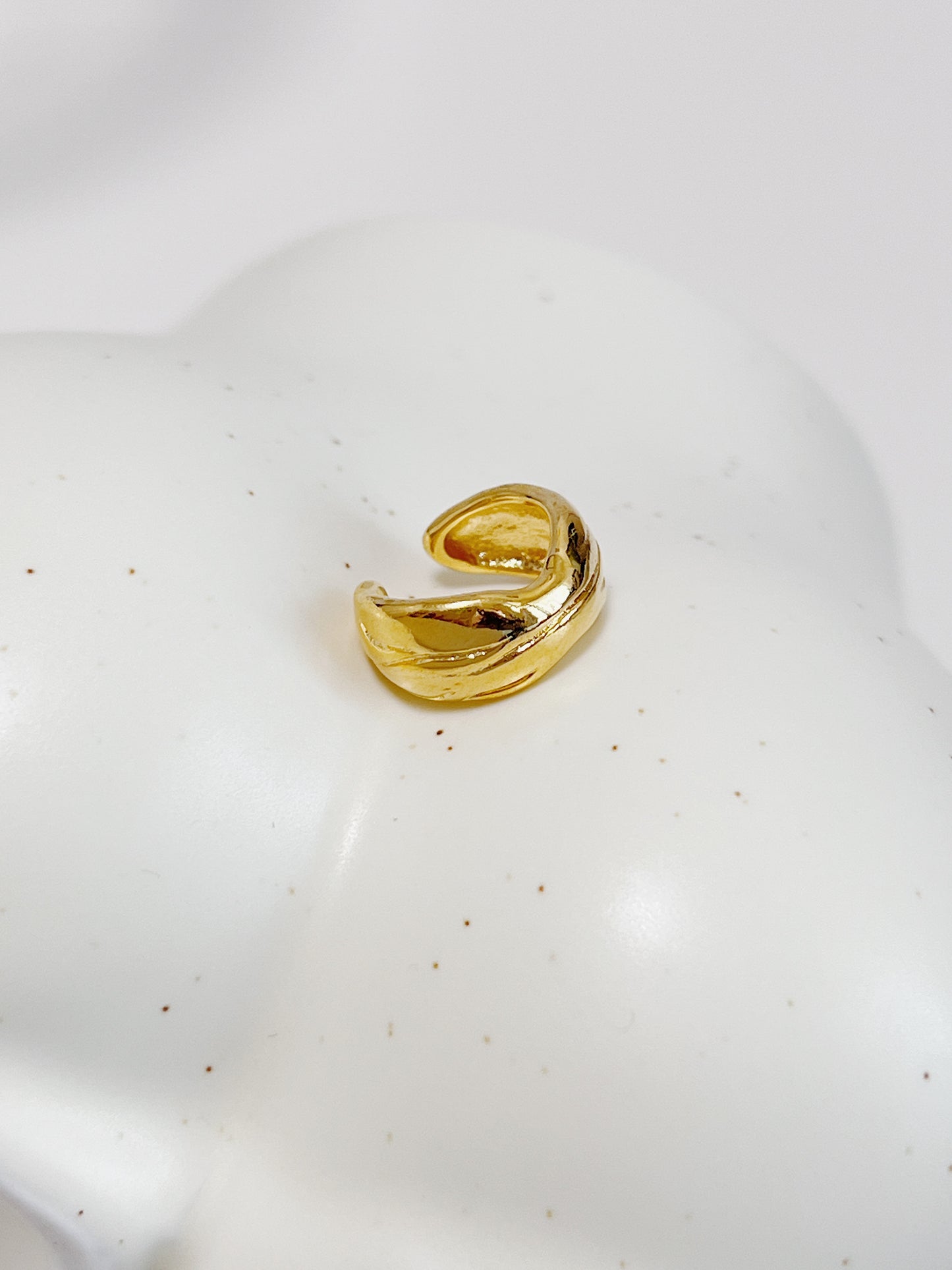 Gold textured ear cuff on a white ceramic plate