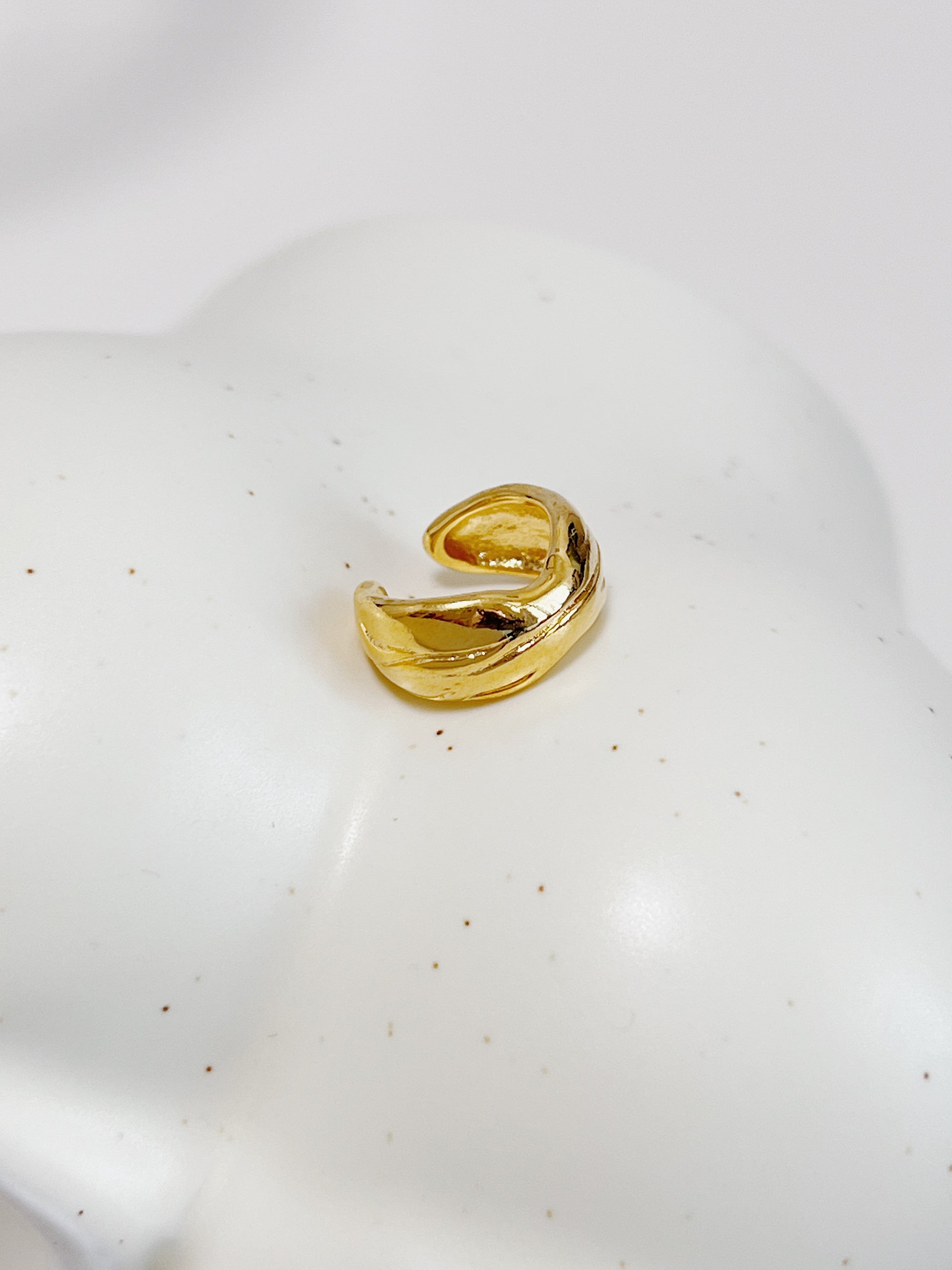 Gold textured ear cuff on a white ceramic plate