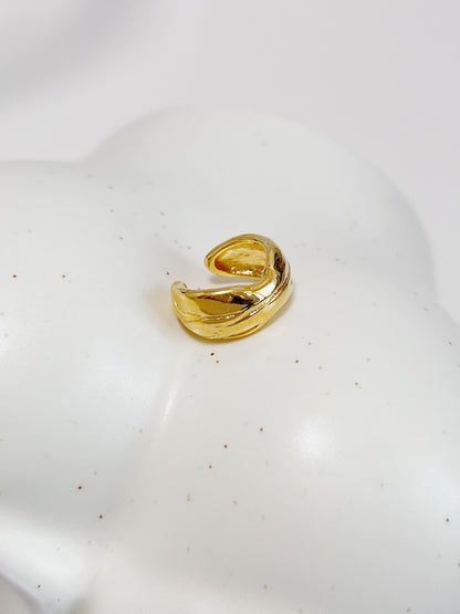 Gold textured ear cuff on a white ceramic plate