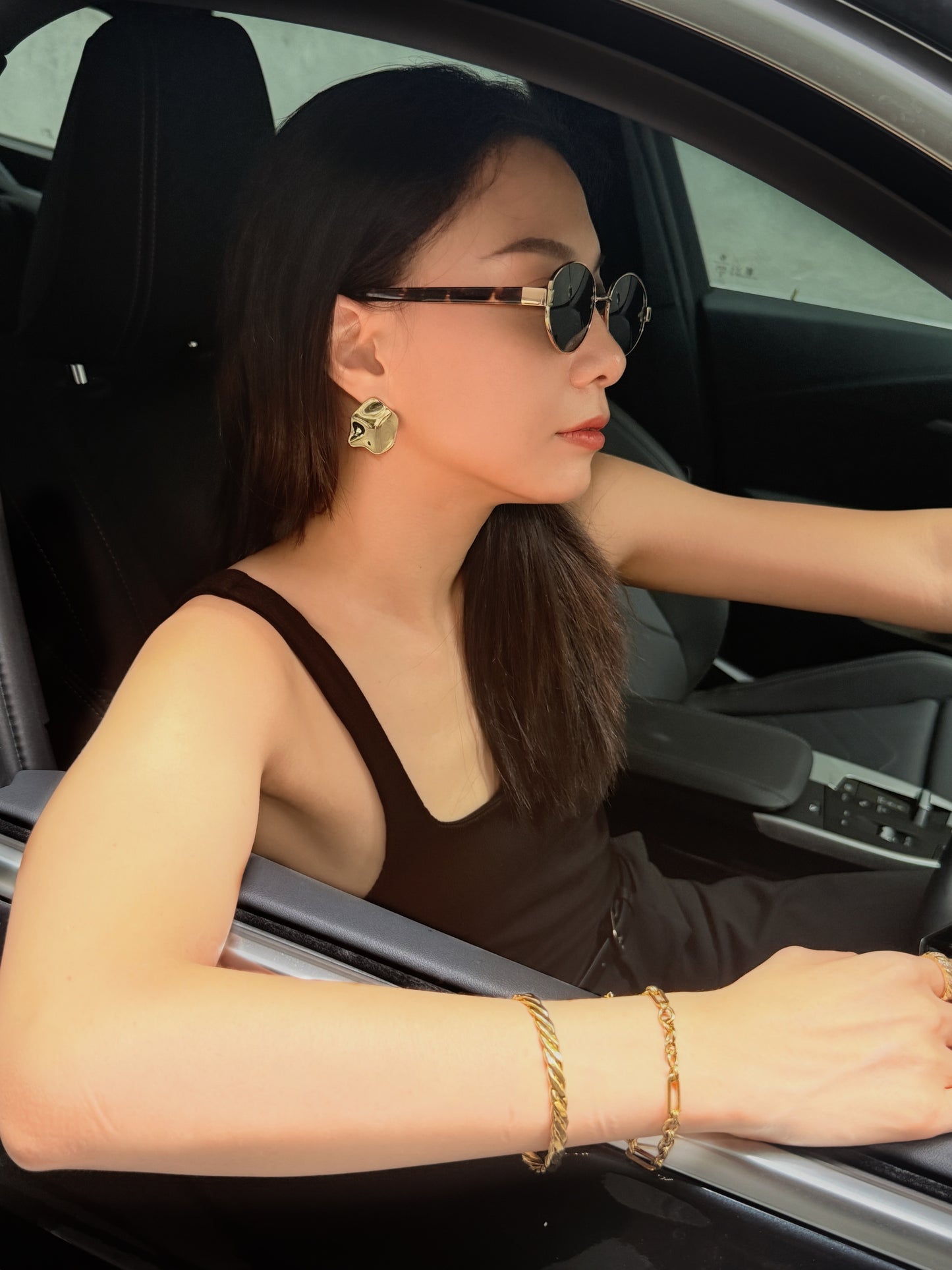Woman sitting in a car wearing sunglasses and gold jewelry