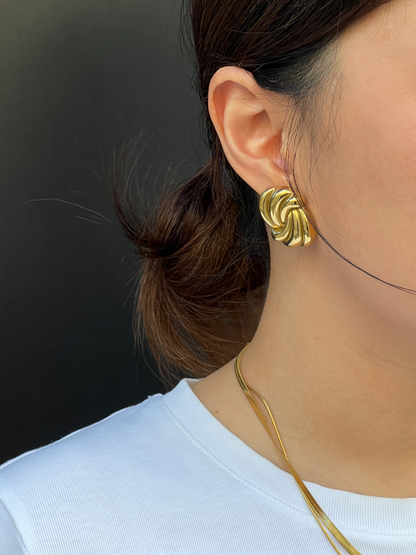 Statement gold twist earring worn by a person with a plain background