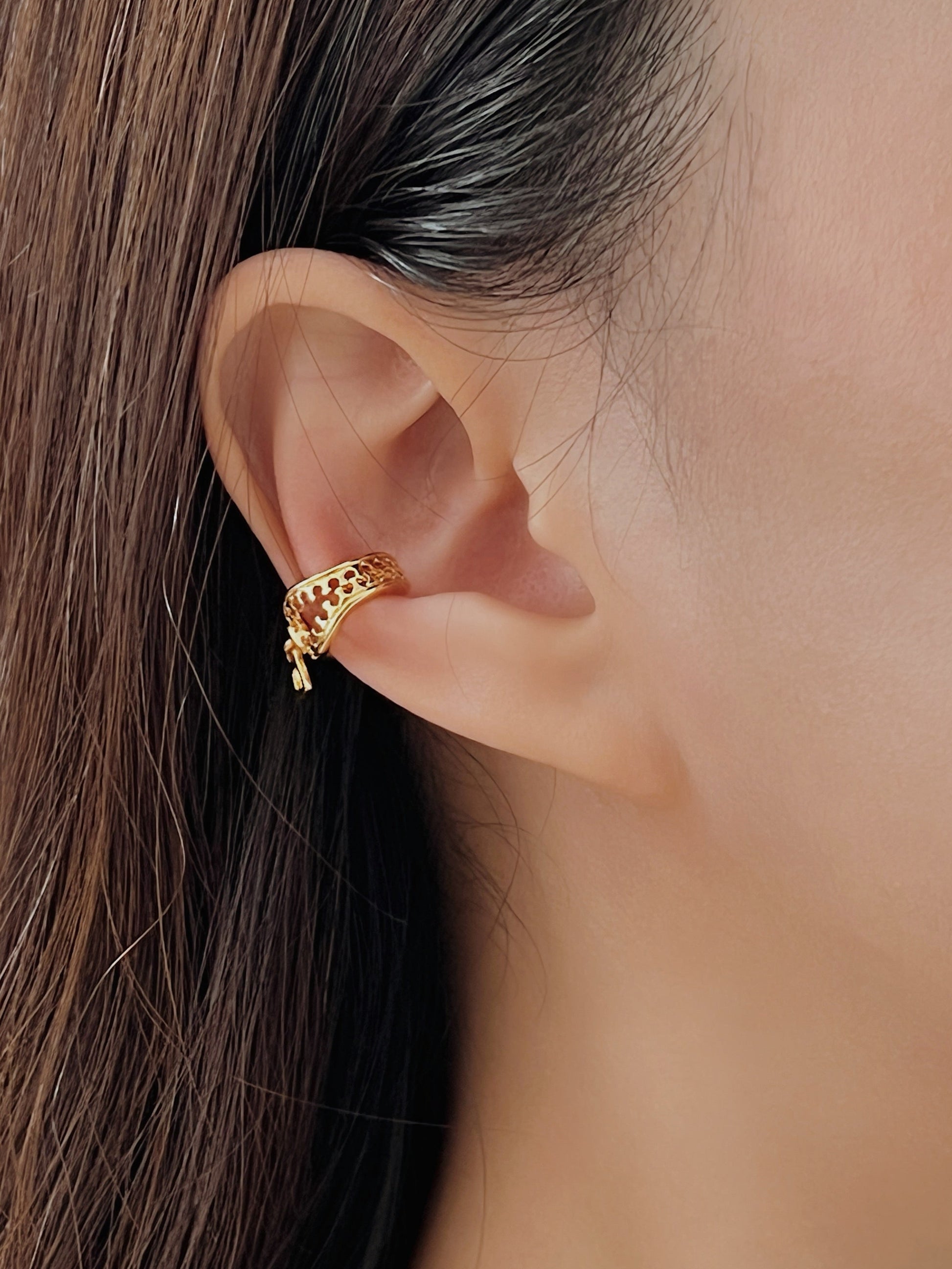 Close-up of a person wearing a gold zipper ear cuff with a small zipper pull.