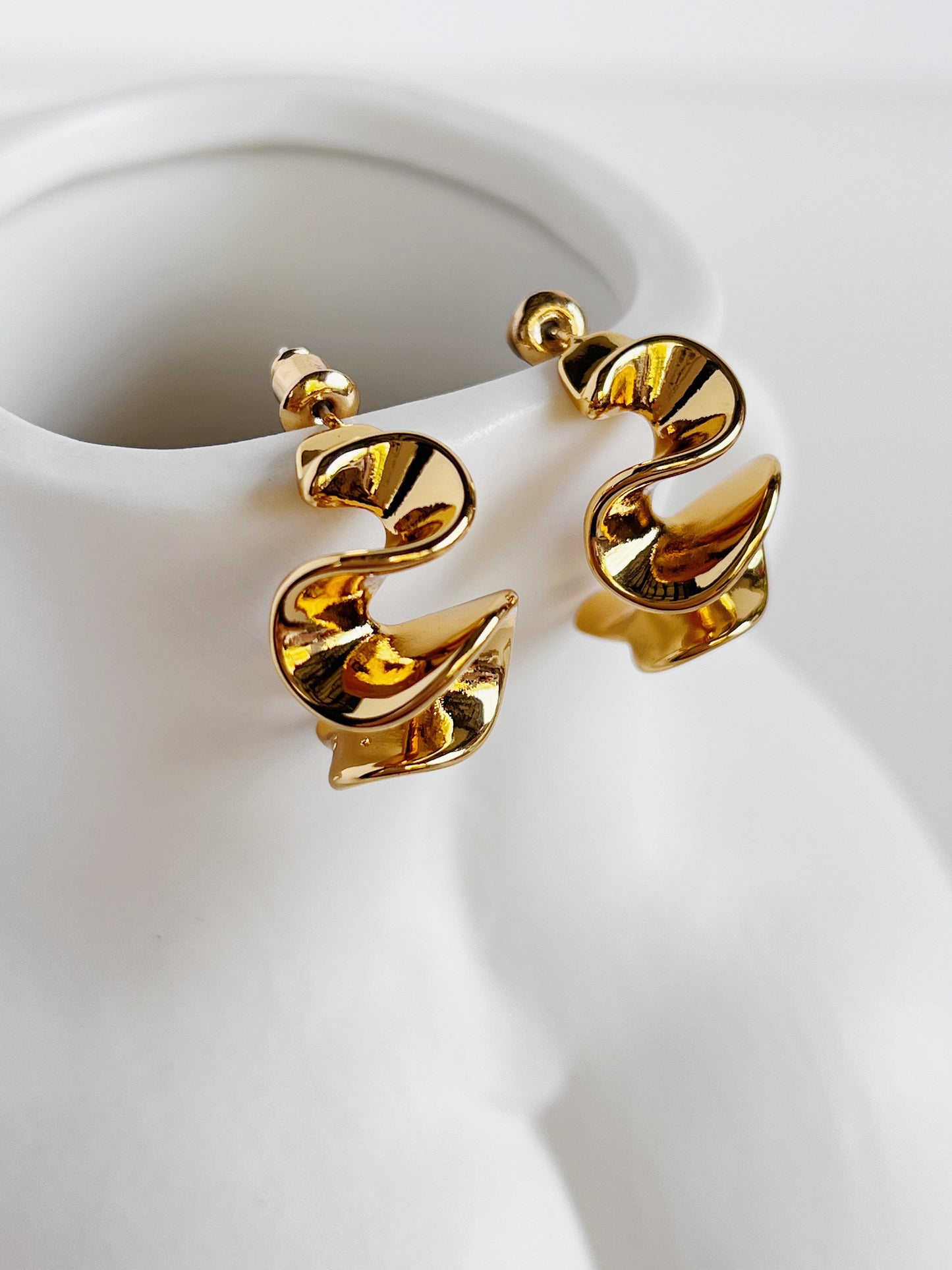 Gold spiral earrings on a white ceramic stand