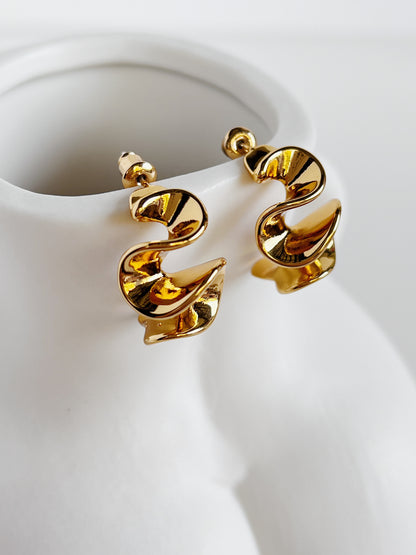 Gold spiral earrings on a white ceramic stand