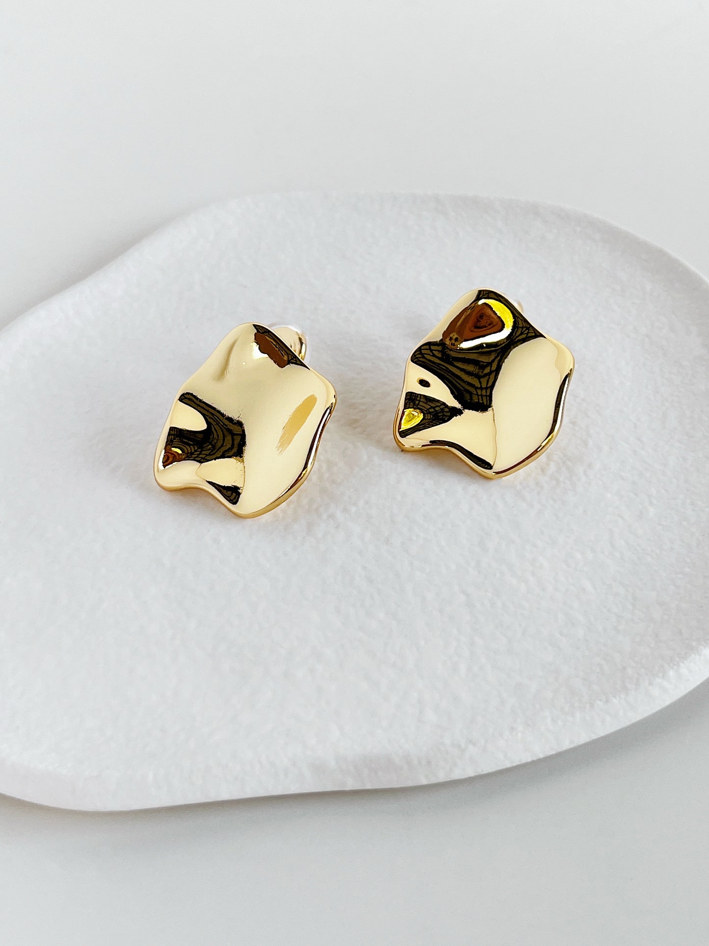 Gold crumpled clip on earrings on a white dish