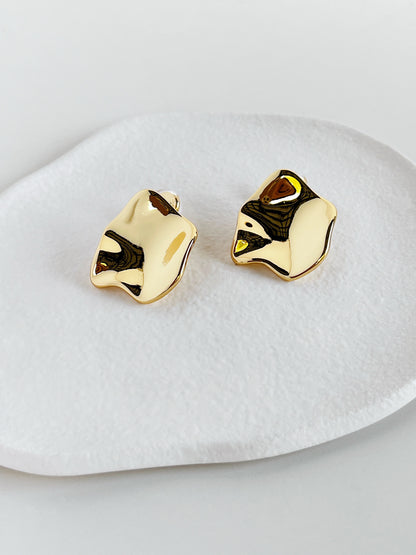 Gold crumpled clip on earrings on a white dish