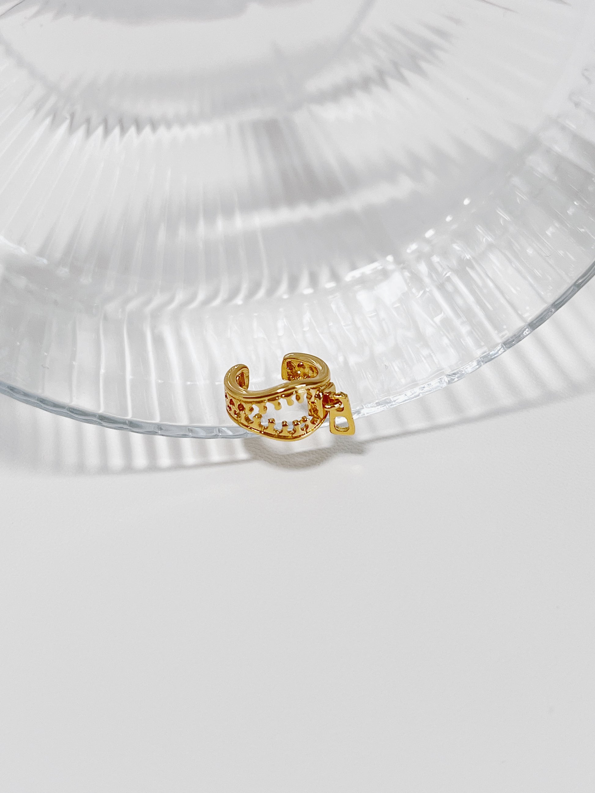 Gold zipper design ear cuff on a clear glass surface with a white background