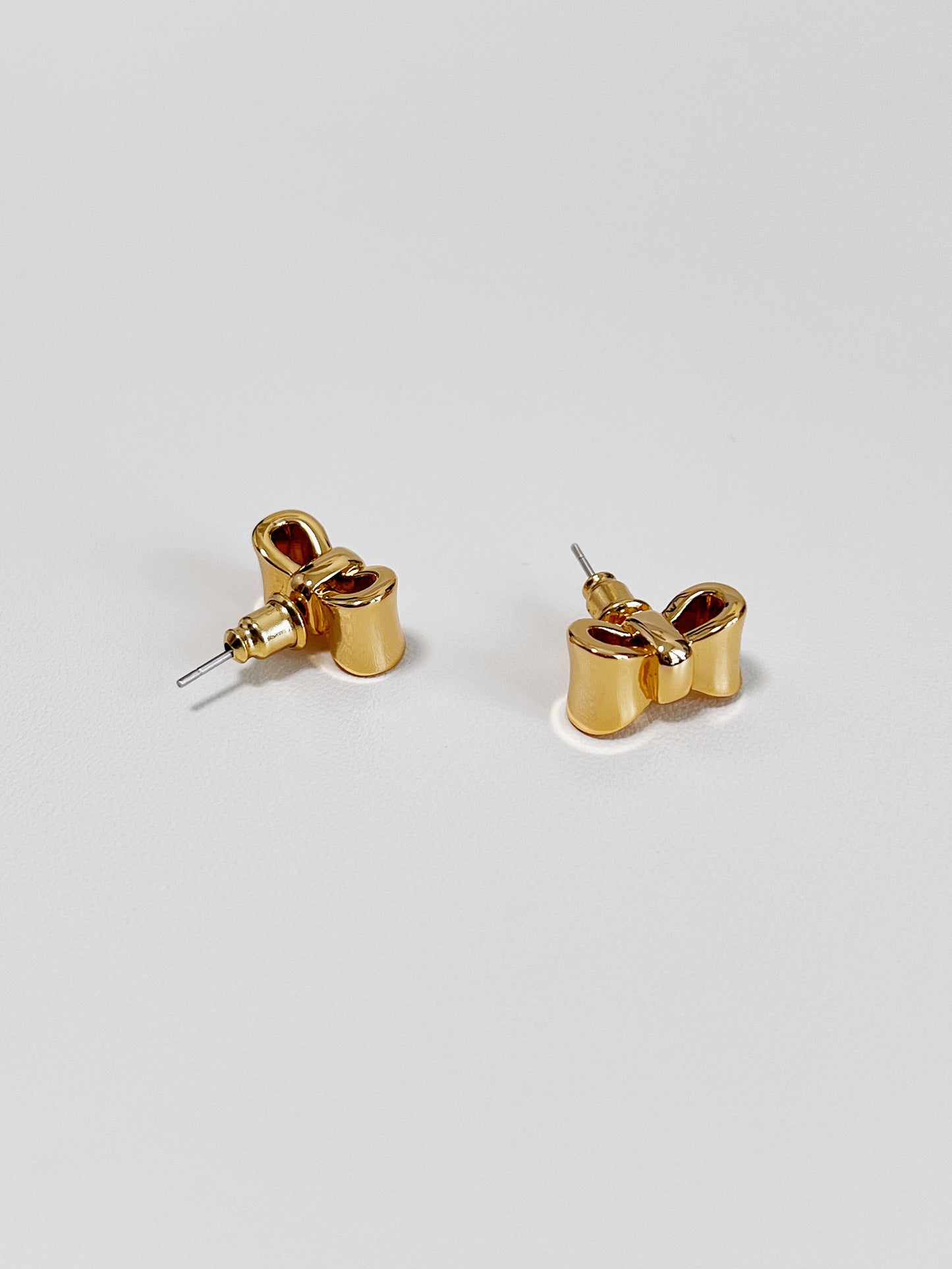 Gold bow-shaped earrings on a light gray background