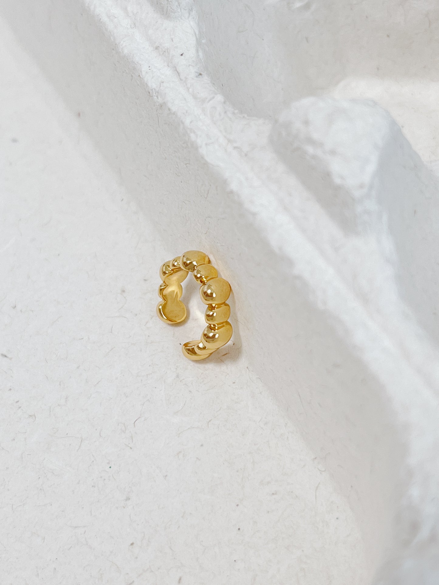 Gold cuff earring on a white textured background