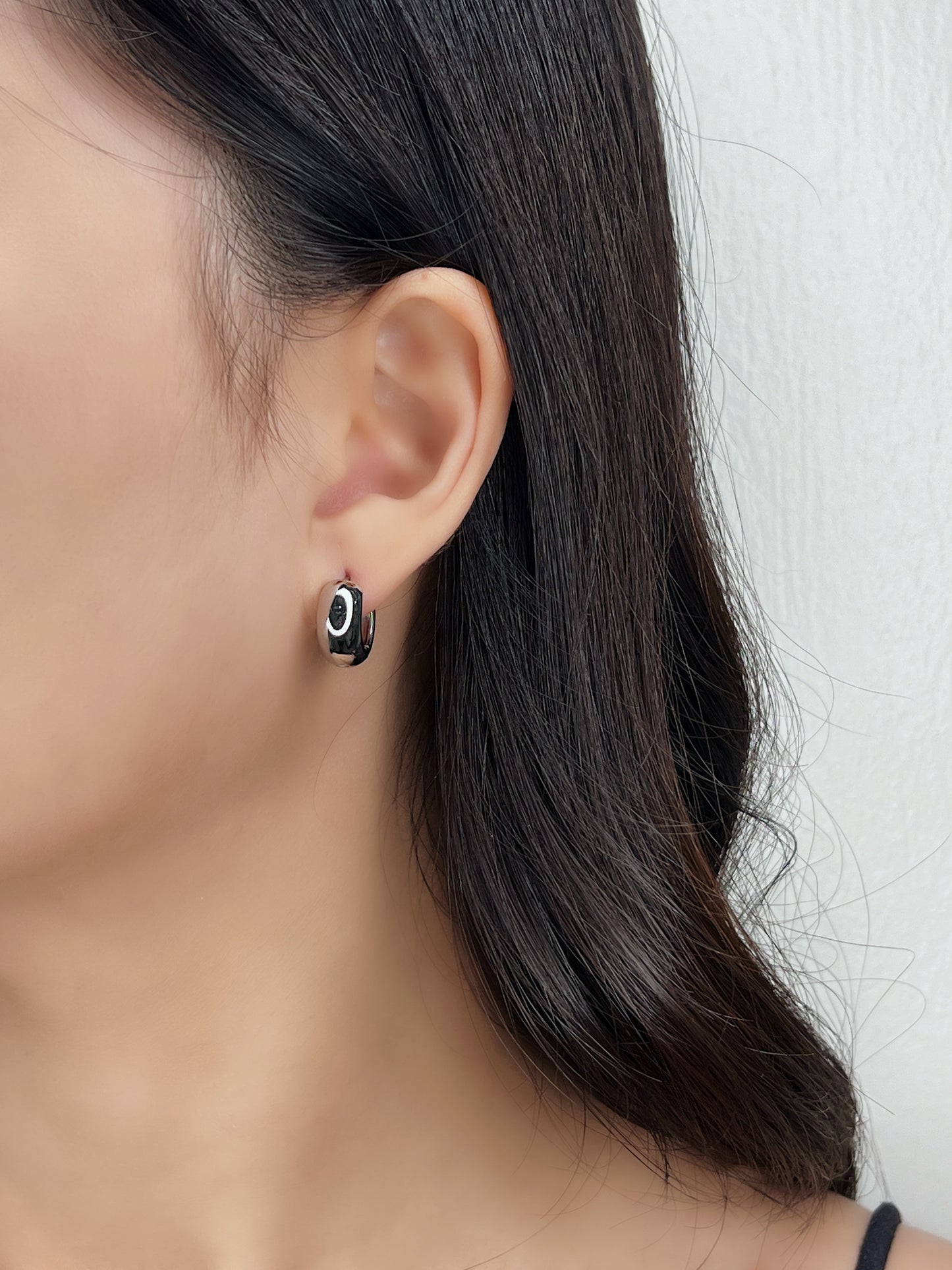 Close-up of an ear wearing a silver huggie hoop earring with a white background