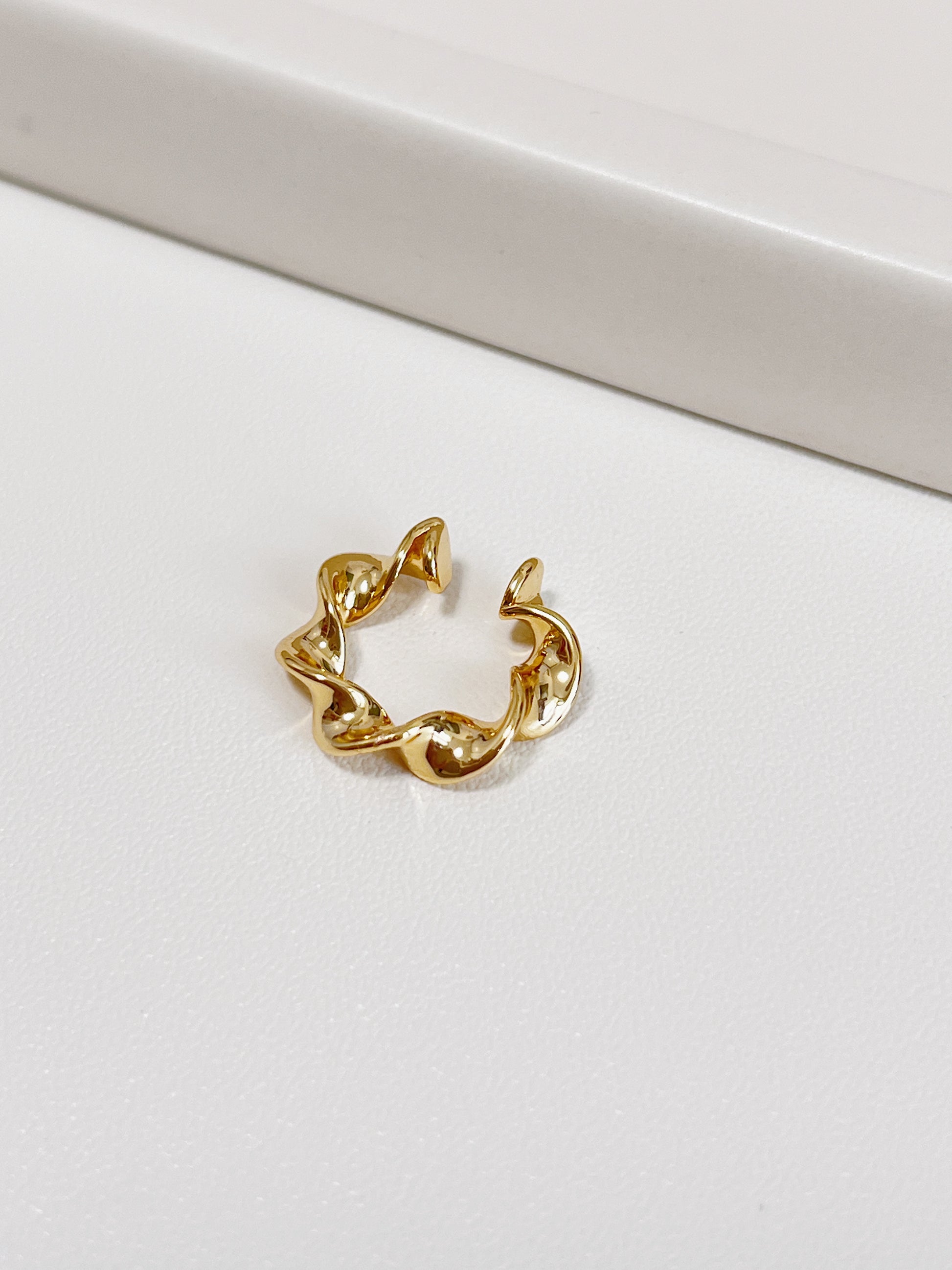 Gold twist ear cuff on a white surface
