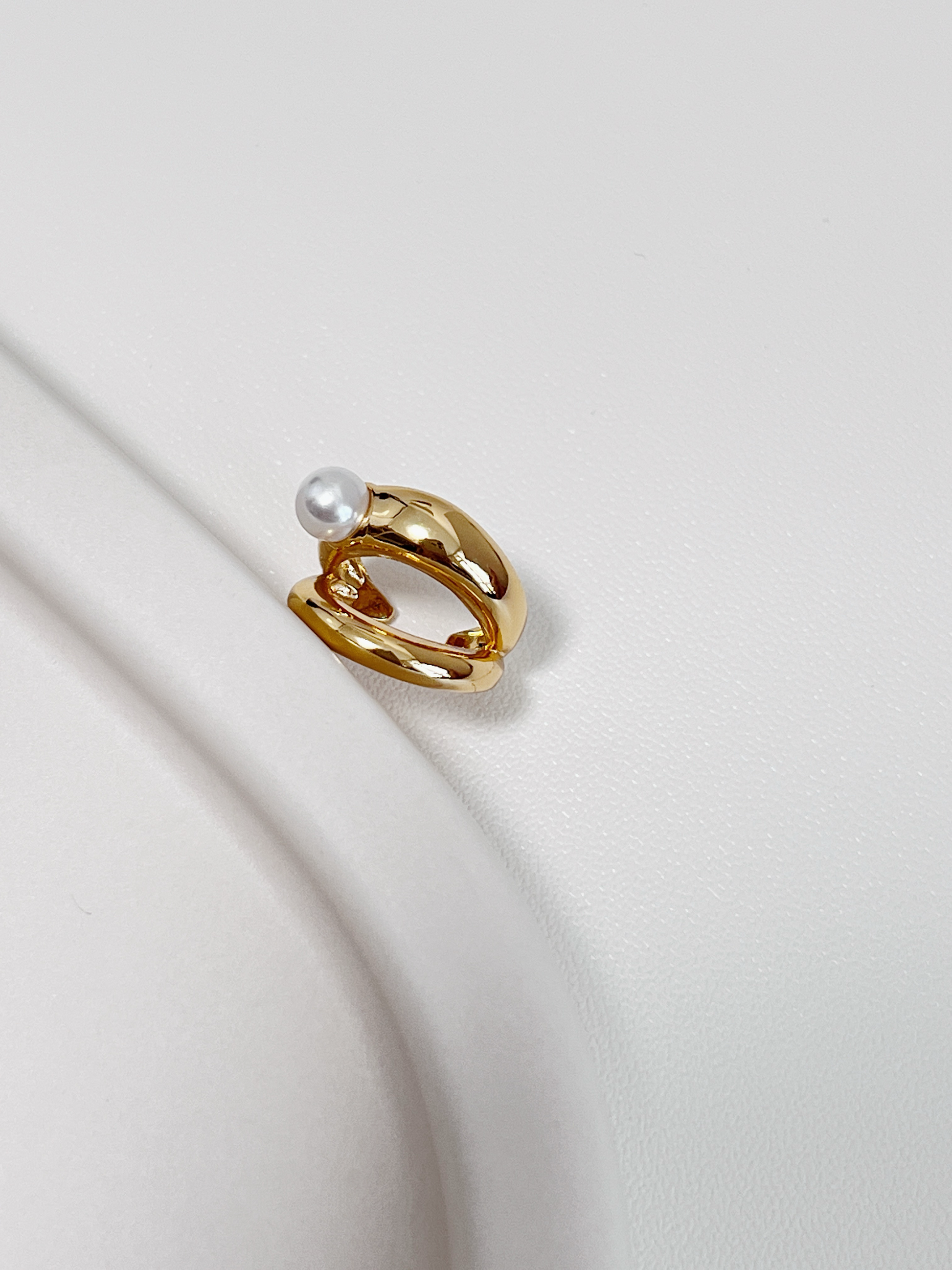 Gold ear cuff with a pearl on a light background