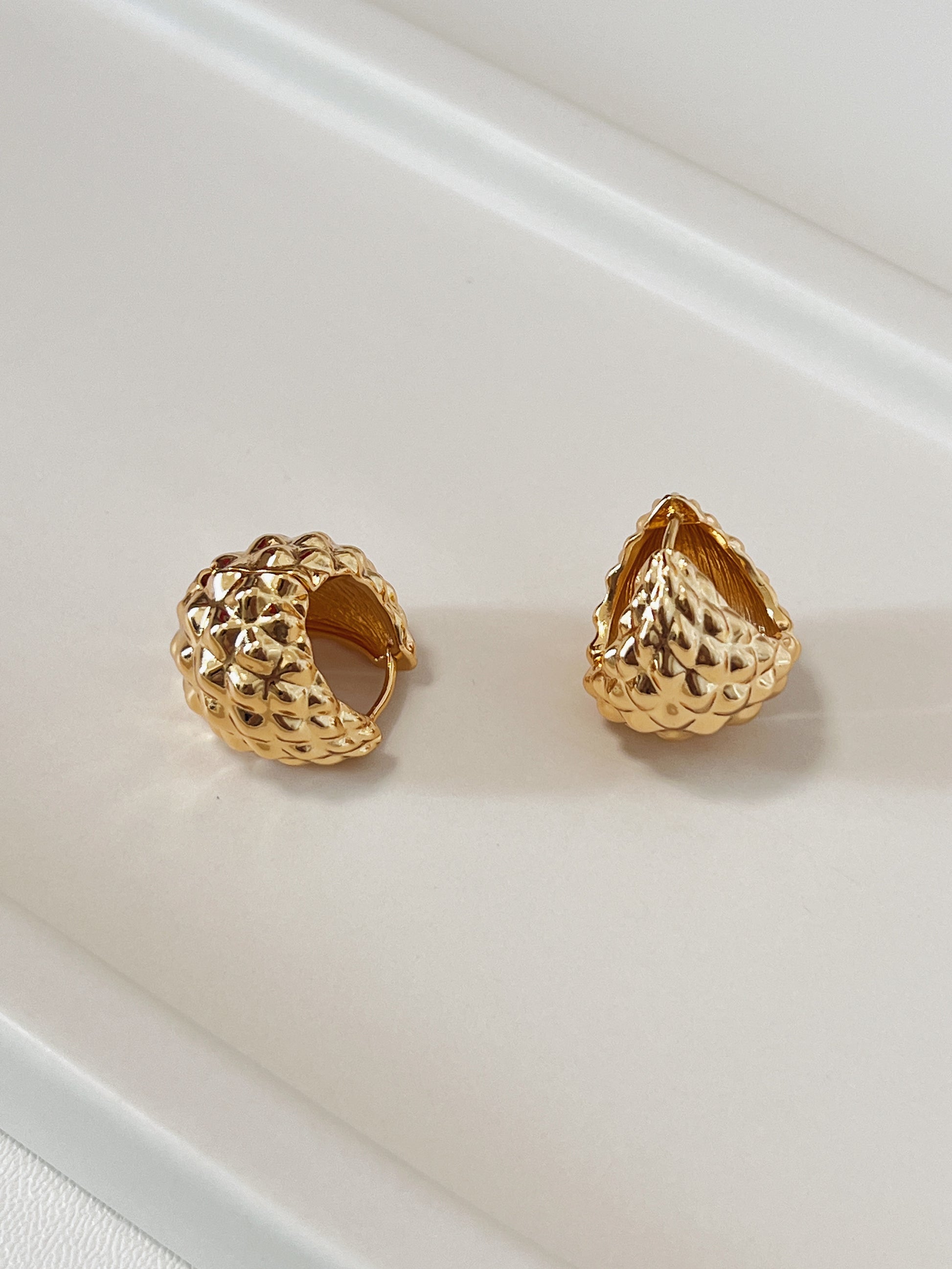 Two gold textured hoop earrings on a light beige surface